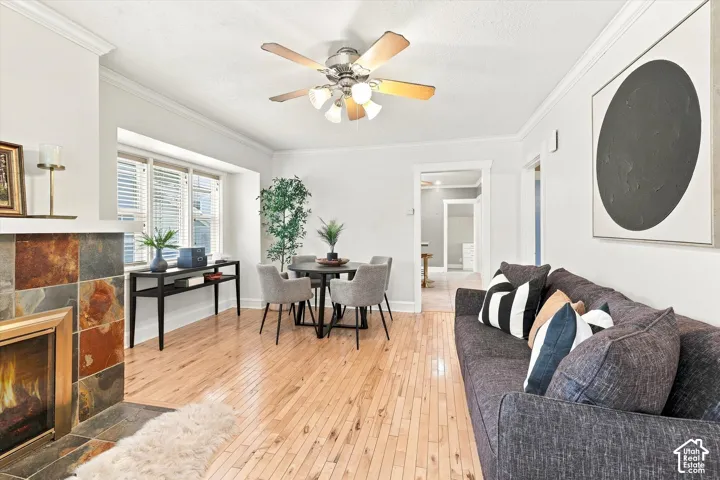 Bright and spacious living area showcasing gleaming wood-finish flooring, a gas fireplace with decorative tile surround, and a ceiling fan with integrated lighting