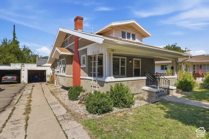 Craftsman-style home featuring a covered front porch, stucco exterior, and a prominent red brick chimney