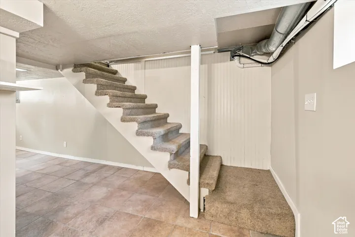 Finished basement featuring open-concept layout with wood-finish flooring, exposed ceiling infrastructure with ductwork, recessed lighting, white drywall construction, and floating staircase with wood treads and white support structure