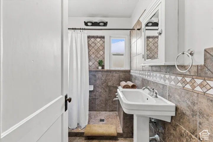 Elegant bathroom featuring a pedestal sink with chrome fixtures, decorative tile backsplash in neutral tones, and a walk-in shower with glass enclosure