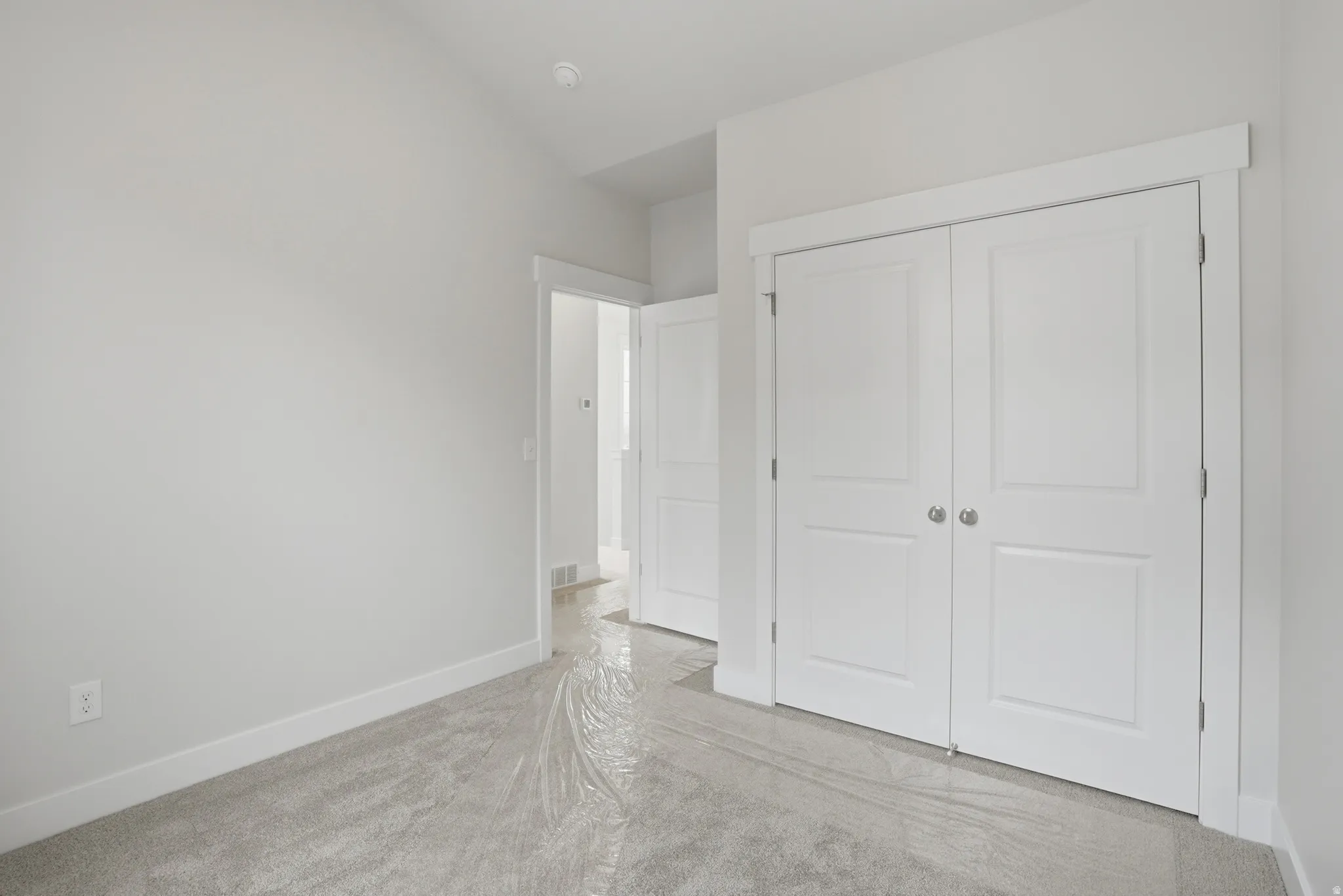 Bright bedroom showcasing elegant double-door white closet with six-panel design, light wood-finish flooring, and clean white walls with neutral trim throughout