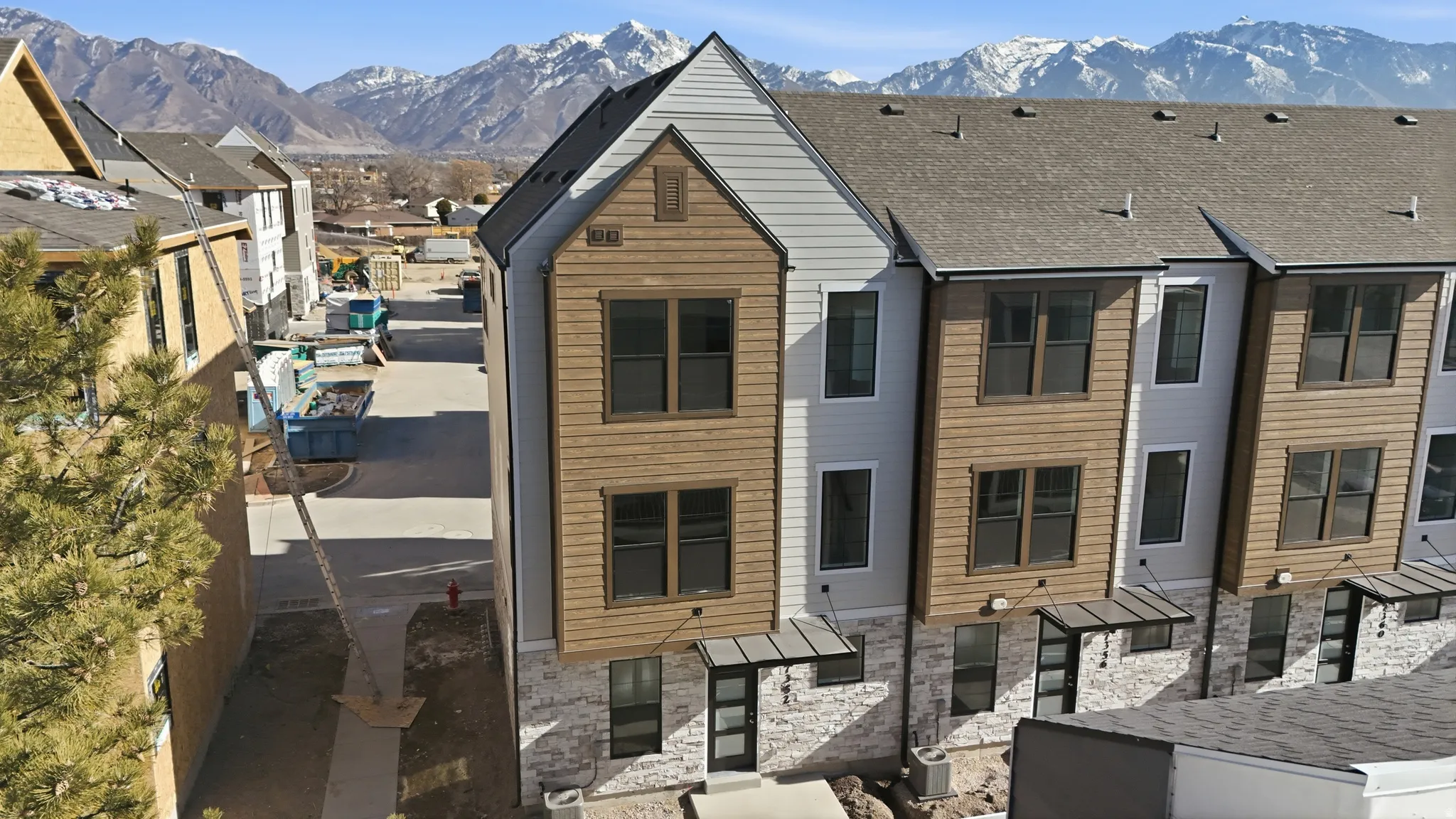 Contemporary townhouse exterior featuring a three-story design, a prominent gable, mixed siding, a stone veneer base, and a pitched roof