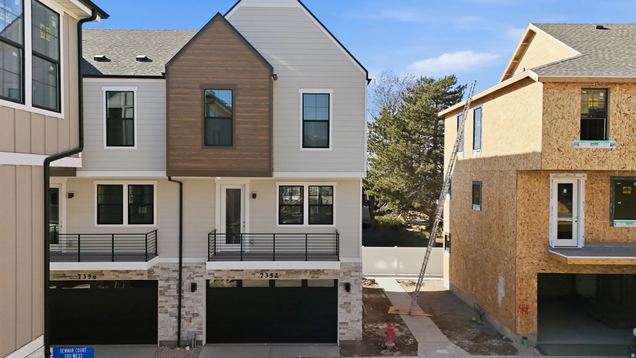 Contemporary townhome exterior featuring light-toned siding, dark trim windows, and a wood-finish accent gable