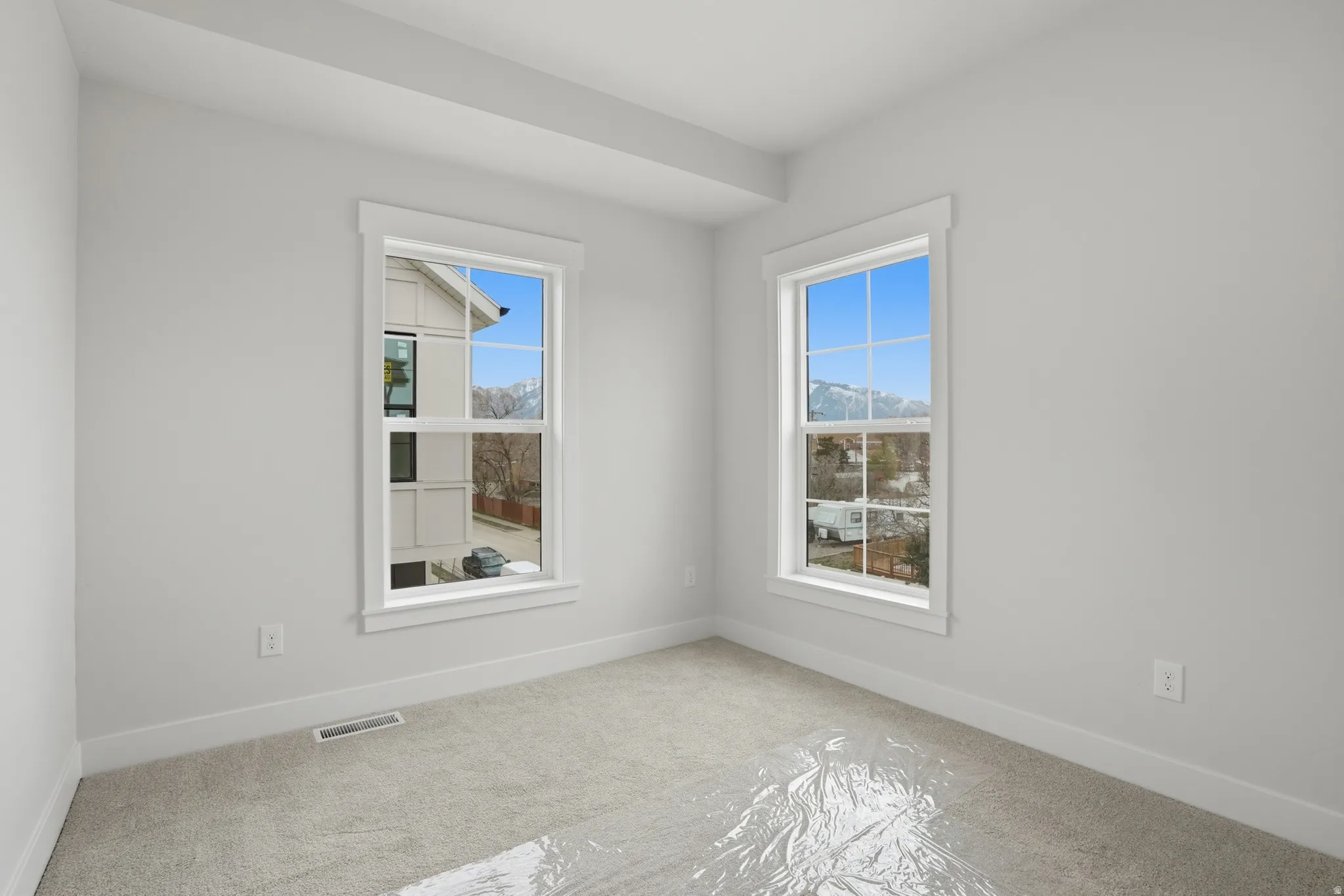Two tall windows with white trim and muntins, light gray wall paint, light gray carpet, and white baseboards