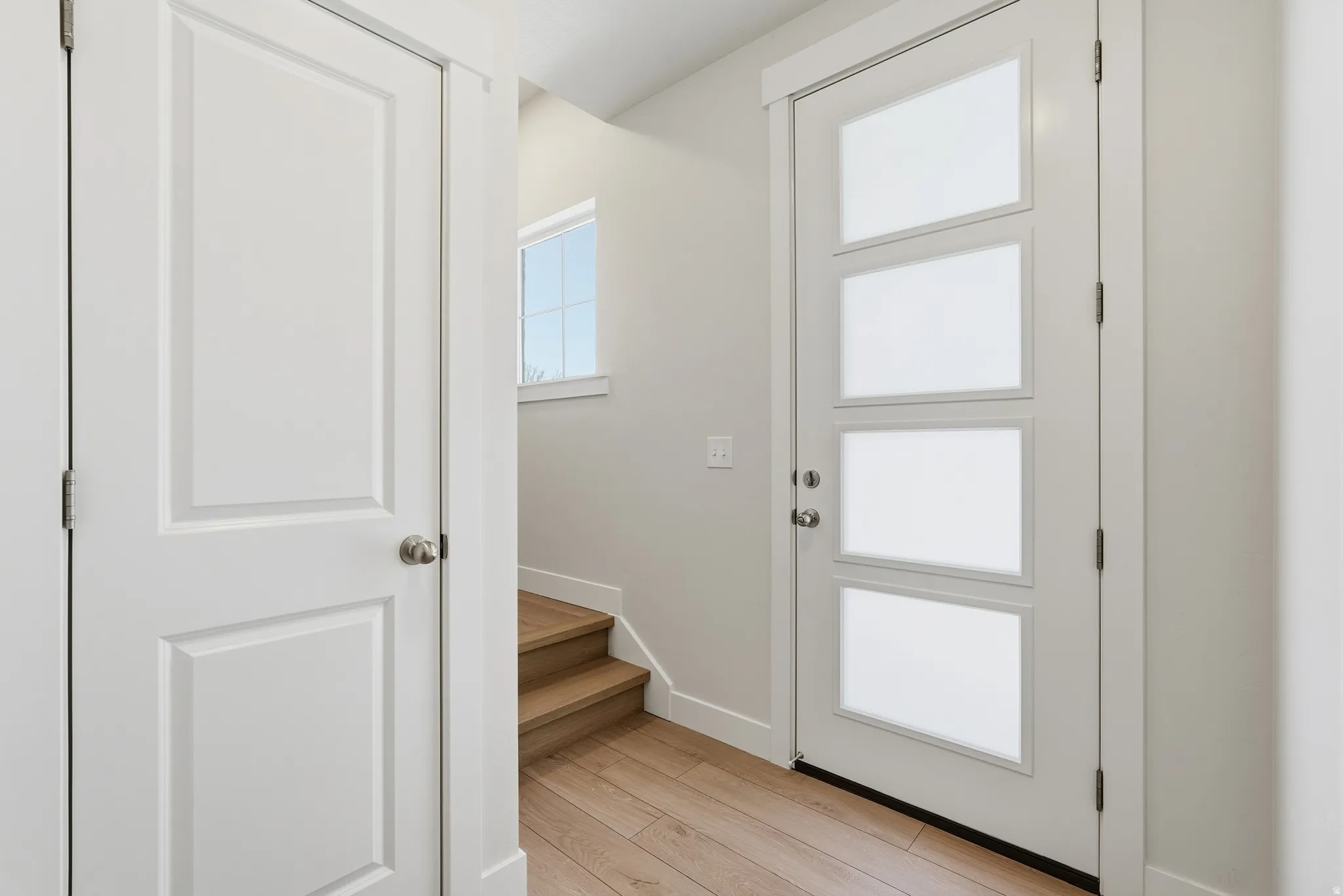 Entryway featuring a modern door with four frosted glass panels, light wood-finish flooring, a white panel door, and staircase with natural wood treads
