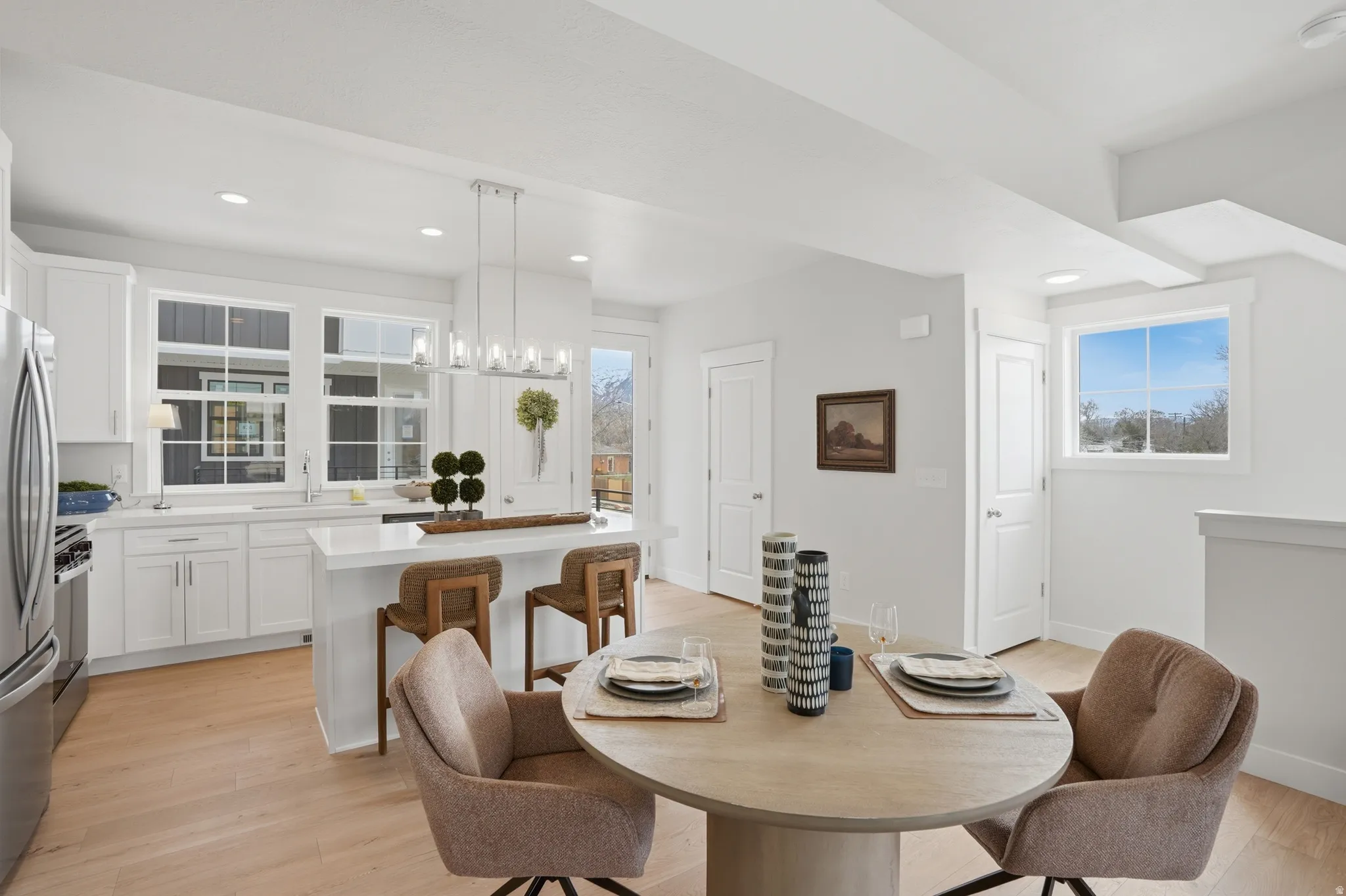 Open-concept living space featuring wood-finish flooring, a contemporary kitchen island with seating, pendant lighting, stainless steel appliances, and white cabinetry