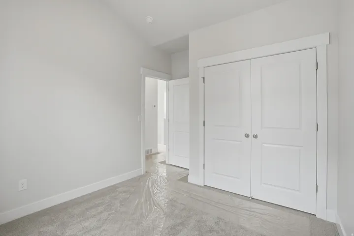 Bright bedroom showcasing elegant double-door white closet with six-panel design, light wood-finish flooring, and clean white walls with neutral trim throughout