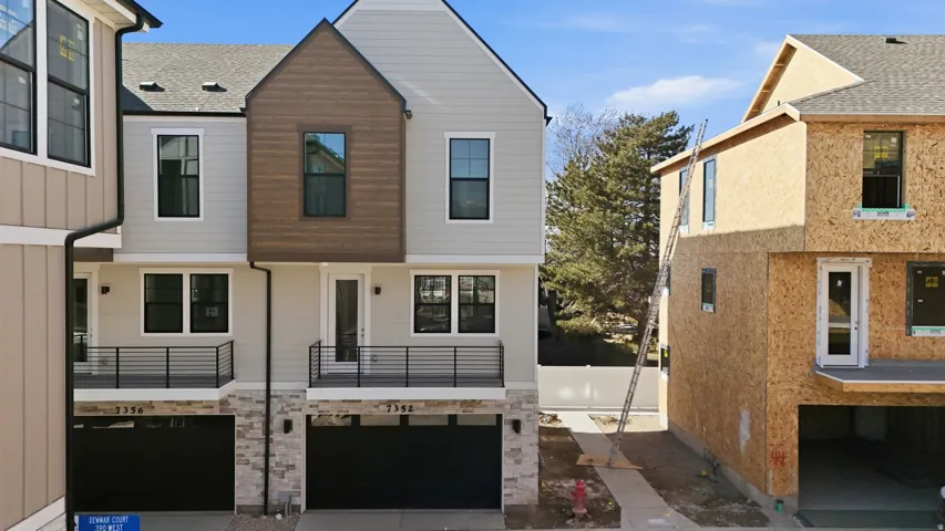 Contemporary townhome exterior featuring light-toned siding, dark trim windows, and a wood-finish accent gable