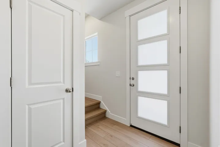 Entryway featuring a modern door with four frosted glass panels, light wood-finish flooring, a white panel door, and staircase with natural wood treads