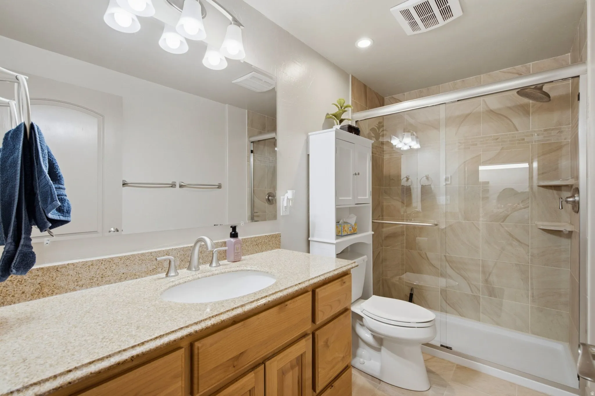 Bathroom featuring a light-toned vanity with an undermount sink, a large mirror, a tiled shower with a clear glass enclosure, and recessed lighting