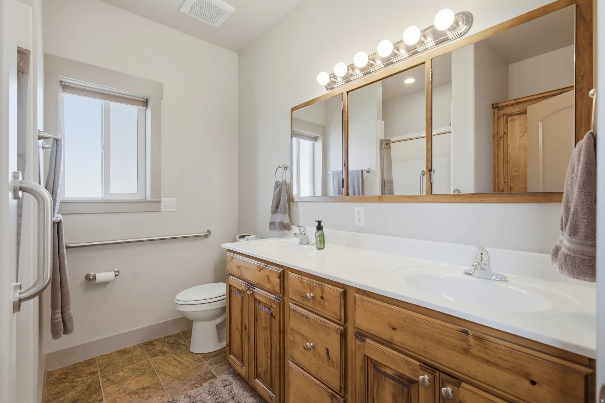 Spacious primary bathroom featuring dual vanity with wood cabinetry, white quartz countertop, and abundant storage