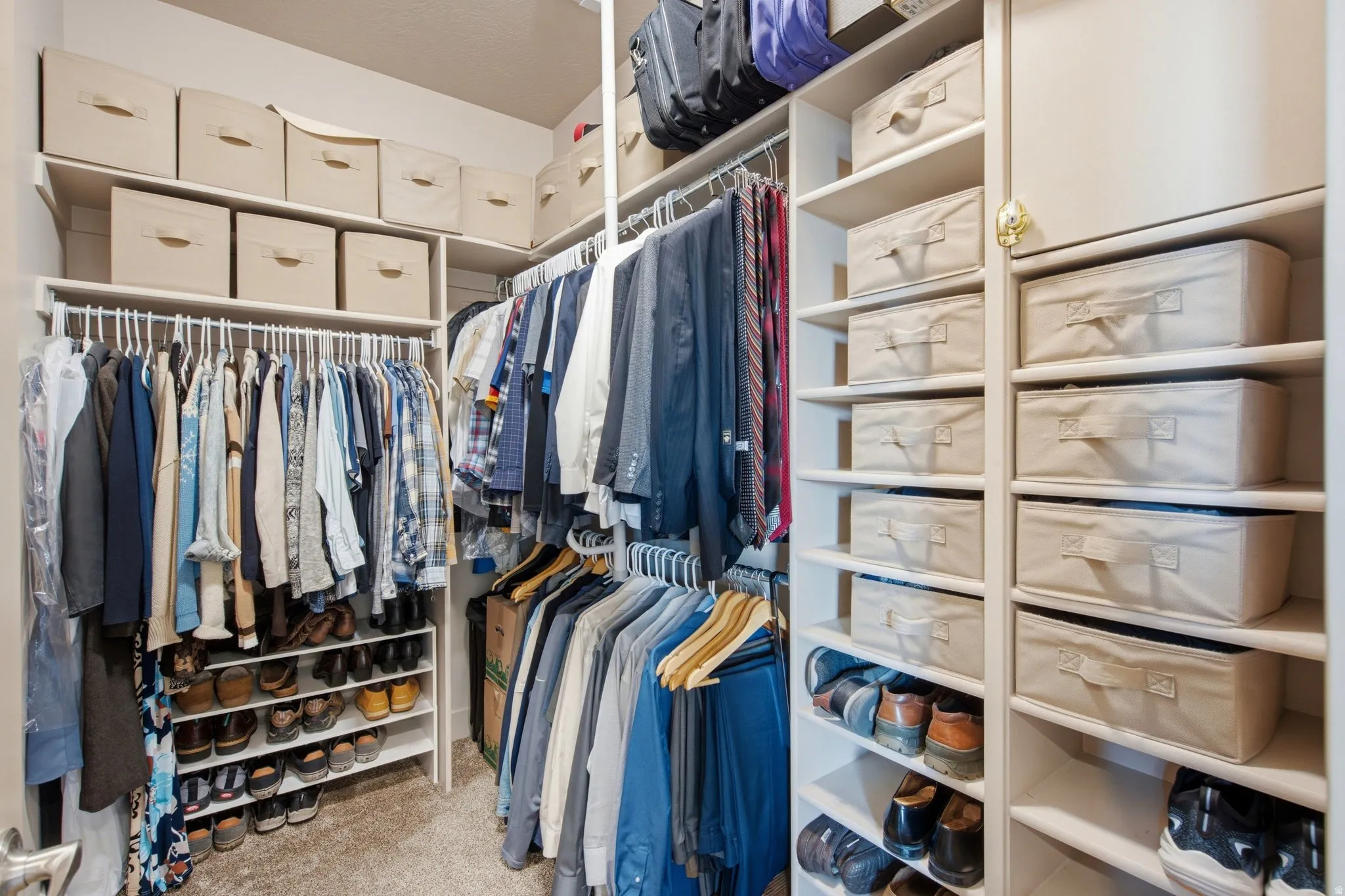 Luxurious walk-in closet featuring dual clothing rods with multiple hanging sections, built-in shelving with woven storage boxes, shoe cubbies with individual compartments, and soft neutral cabinetry throughout