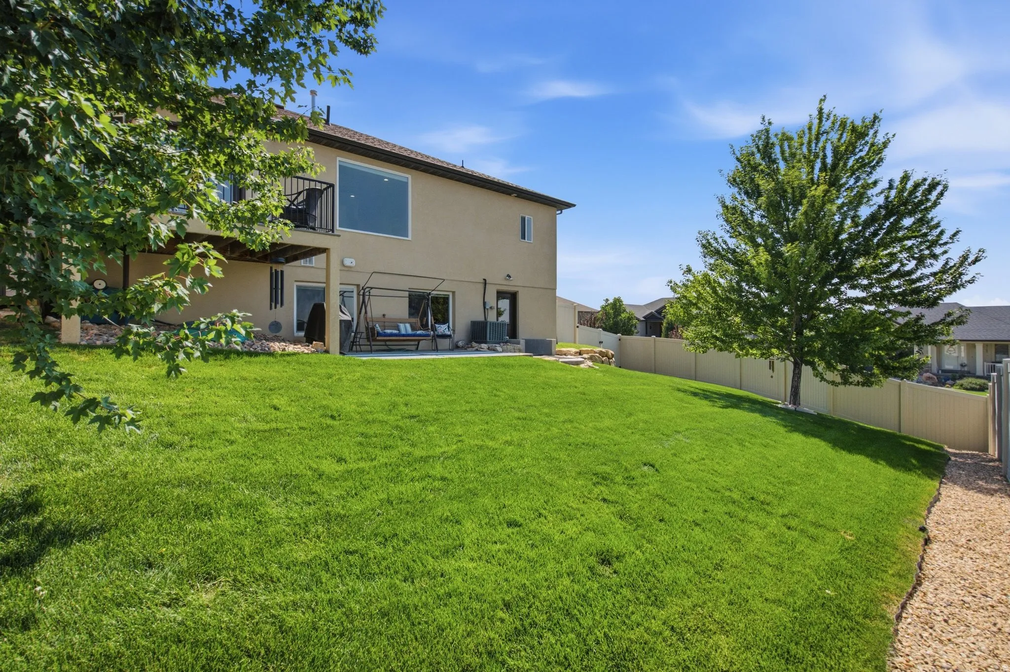 Expansive backyard featuring a manicured lawn, mature shade trees, and decorative gravel hardscaping