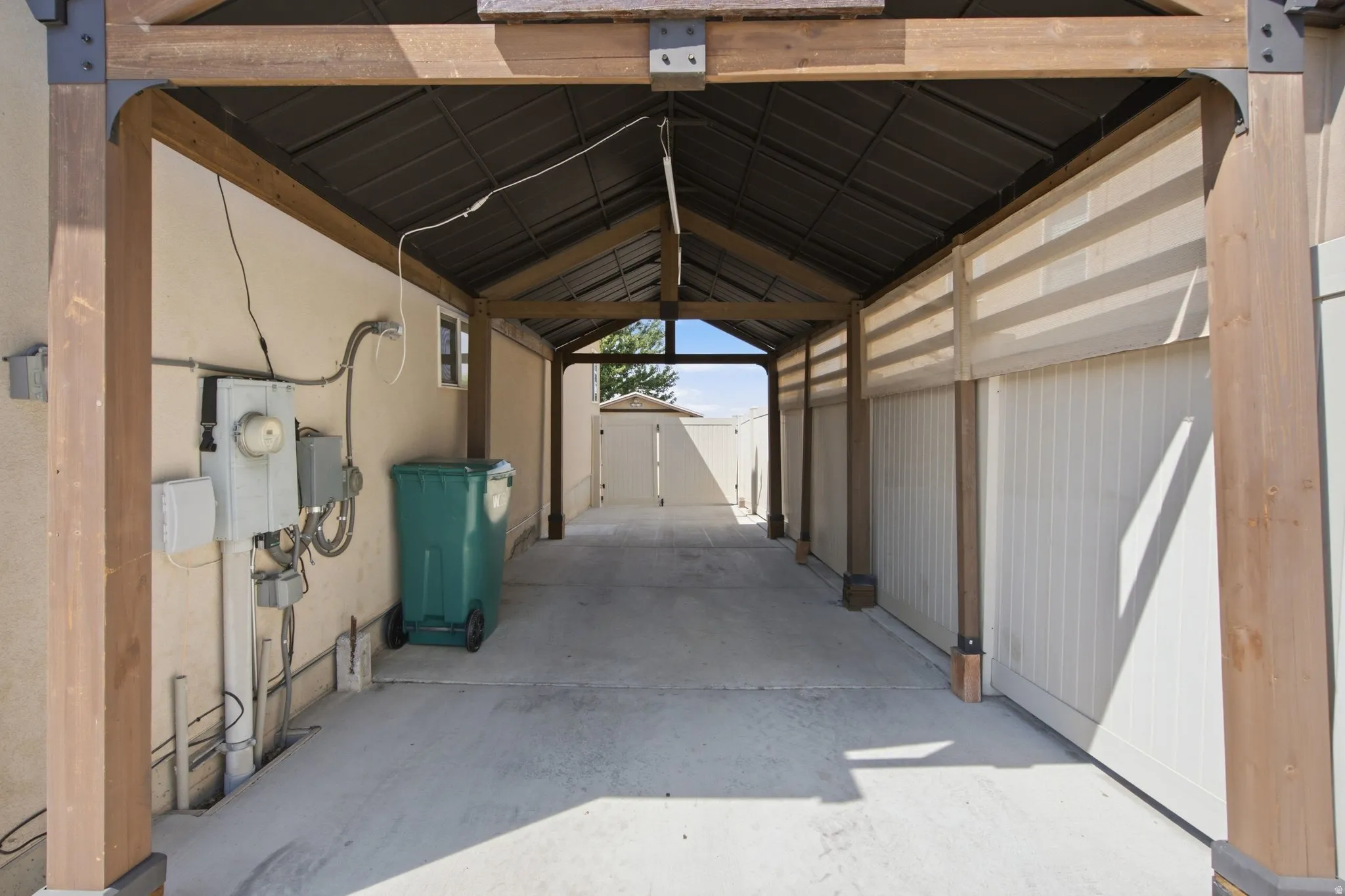 Covered outdoor walkway featuring a concrete surface, a slatted privacy fence, and robust wood-finish support beams with metal accents