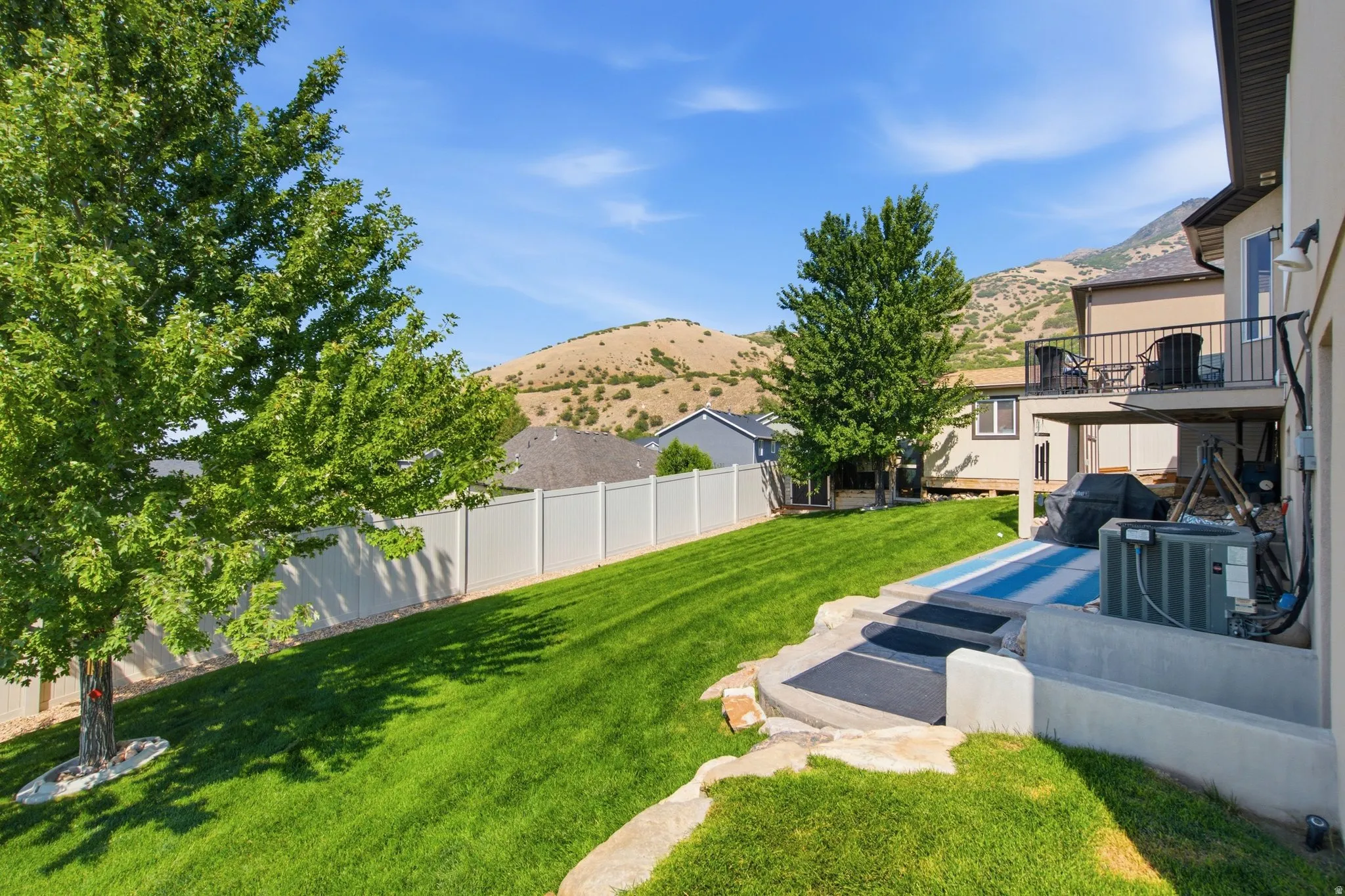 Expansive backyard oasis featuring a meticulously manicured lawn, mature shade trees, and a sunken spa with integrated seating area