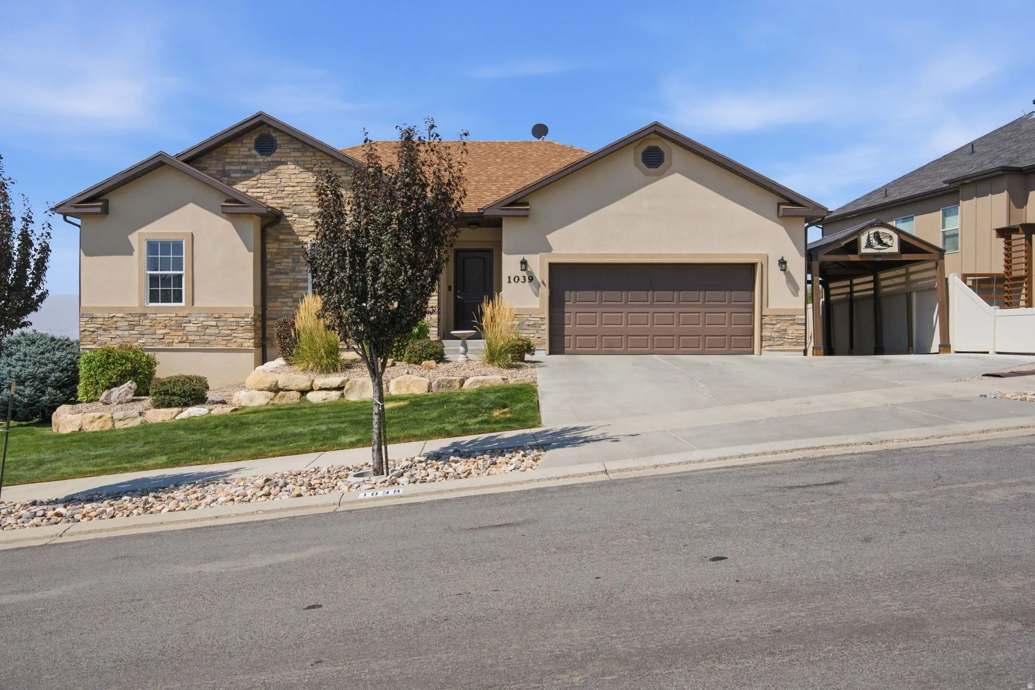Welcoming single-story residence featuring a cream stucco exterior with stone accents, dual gabled rooflines, and a two-car garage with bronze-finish door