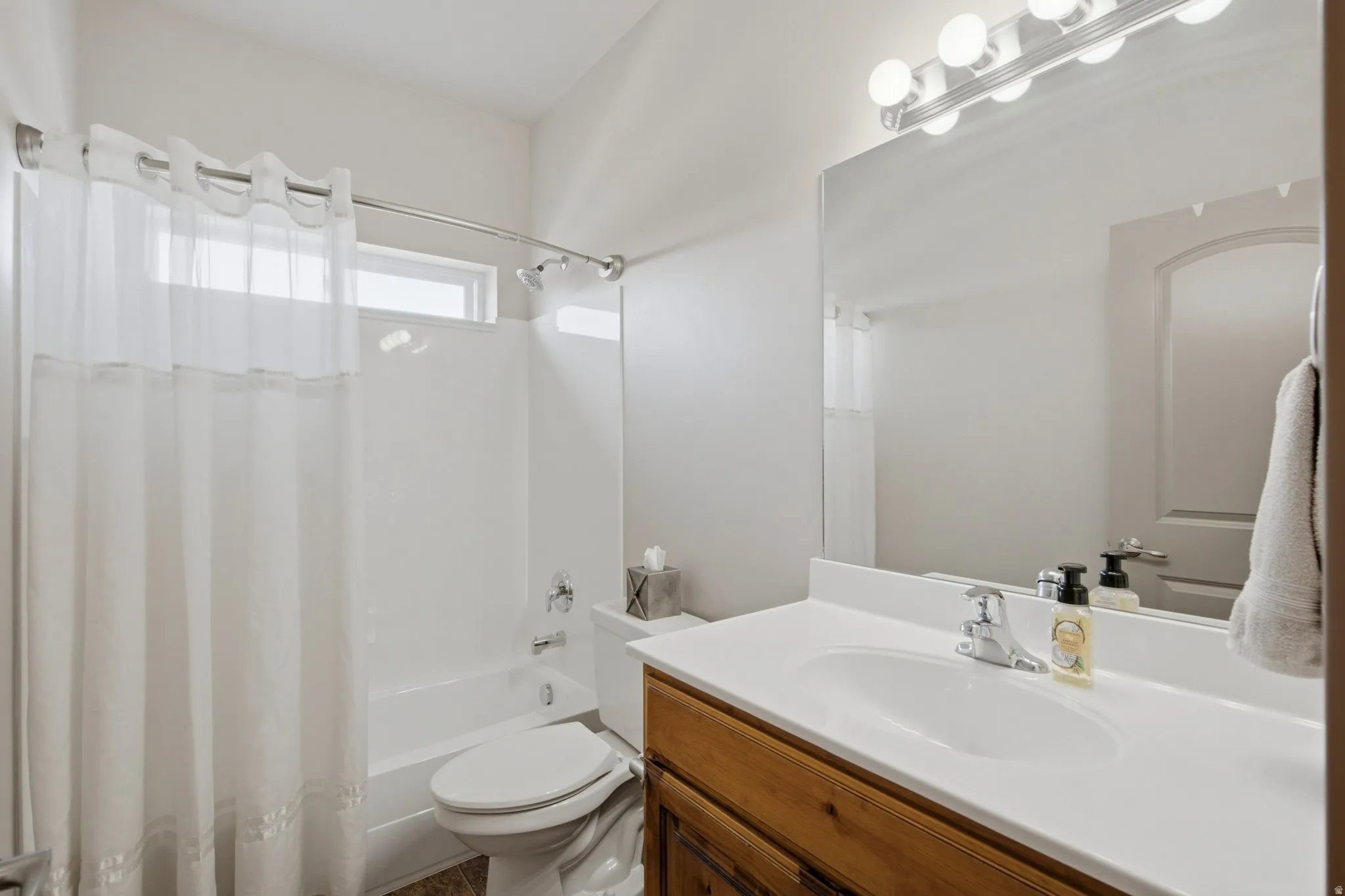 Bright and functional bathroom featuring a wood-finish vanity with a white countertop and dual sink, chrome faucetry, and ample mirror with integrated lighting