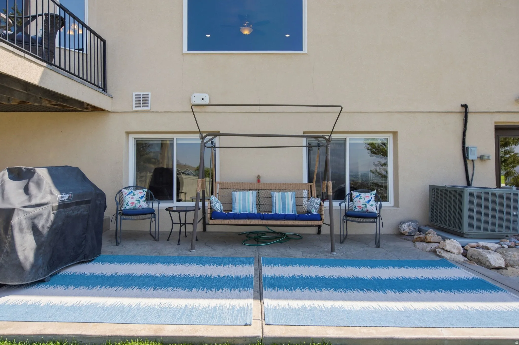 Covered patio with pergola-style overhead structure and striped outdoor rug, featuring built-in seating with blue cushions and coordinating accent pillows
