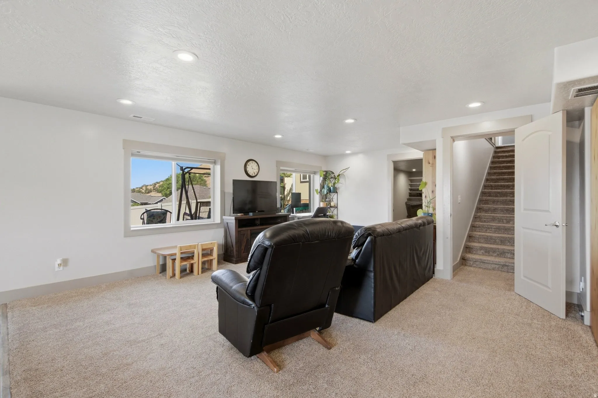 Spacious carpeted room featuring recessed lighting, a window with exterior views, and a doorway leading to a carpeted staircase