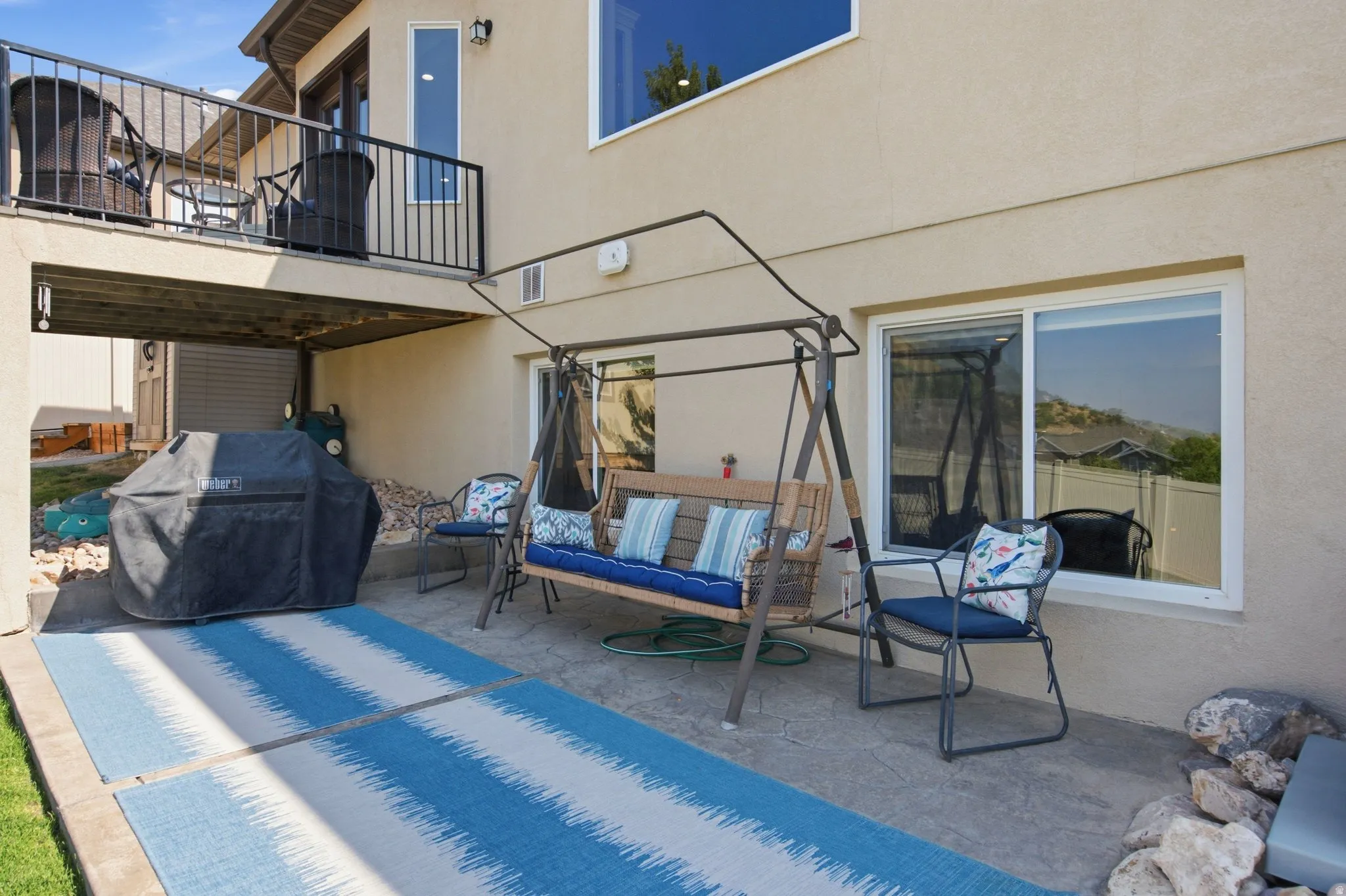 Lower-level patio featuring stamped concrete, stucco exterior, and an upper-level deck with black metal railings