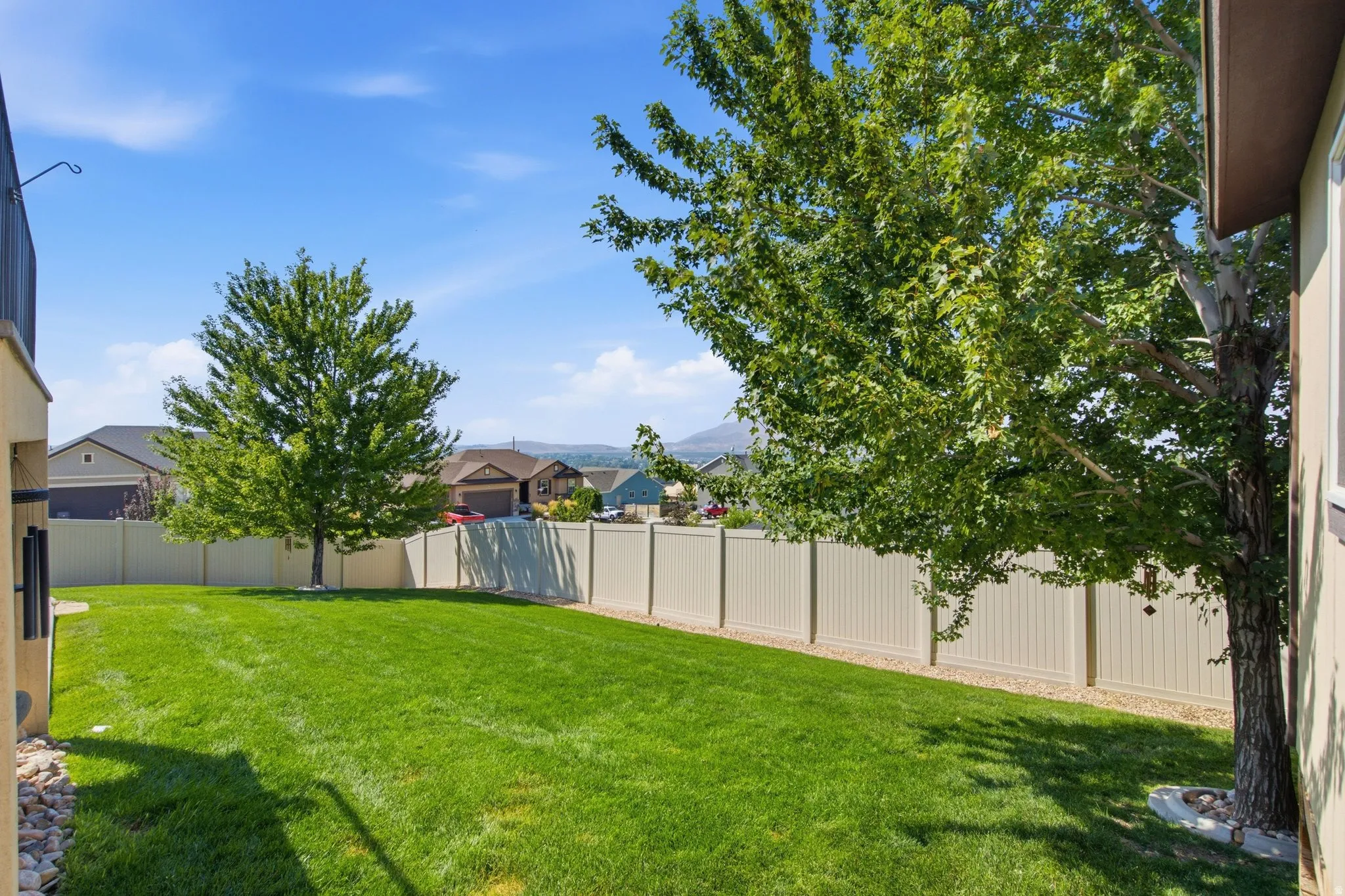 Expansive backyard showcasing a lush, manicured lawn with mature shade trees, vinyl privacy fencing, and mountain vistas in the distance