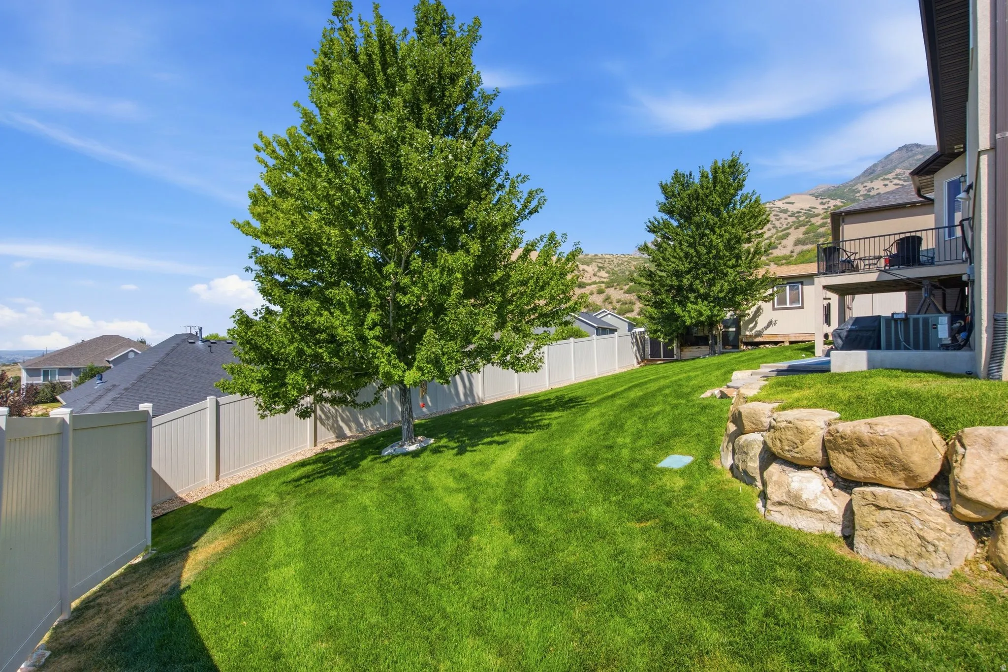 Expansive backyard featuring a meticulously manicured lawn, mature shade trees, and natural stone landscaping elements