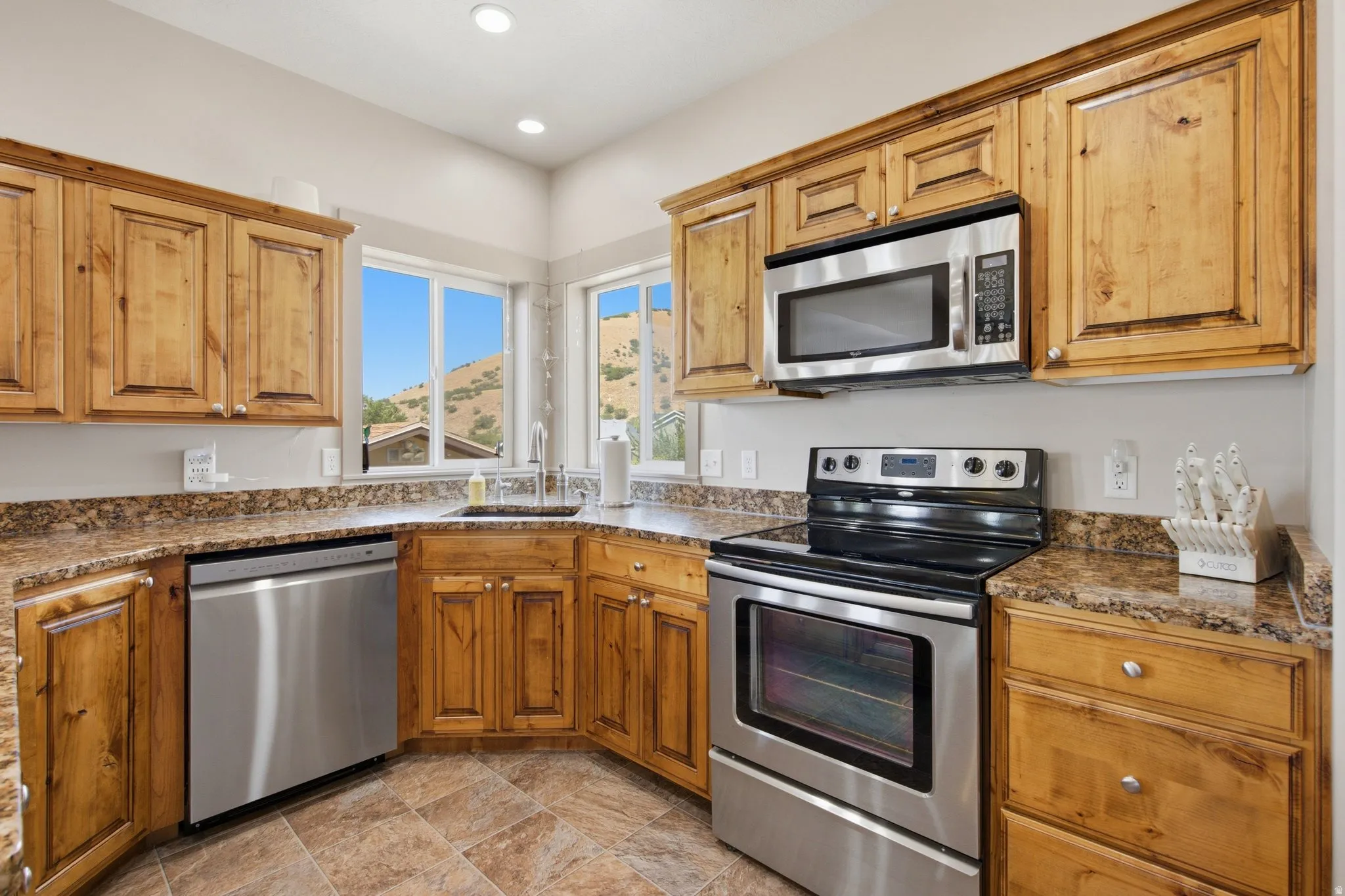 Warm wood cabinetry and stainless steel appliances define this well-appointed kitchen, featuring granite countertops, a black electric range with convection oven, and a stainless steel dishwasher