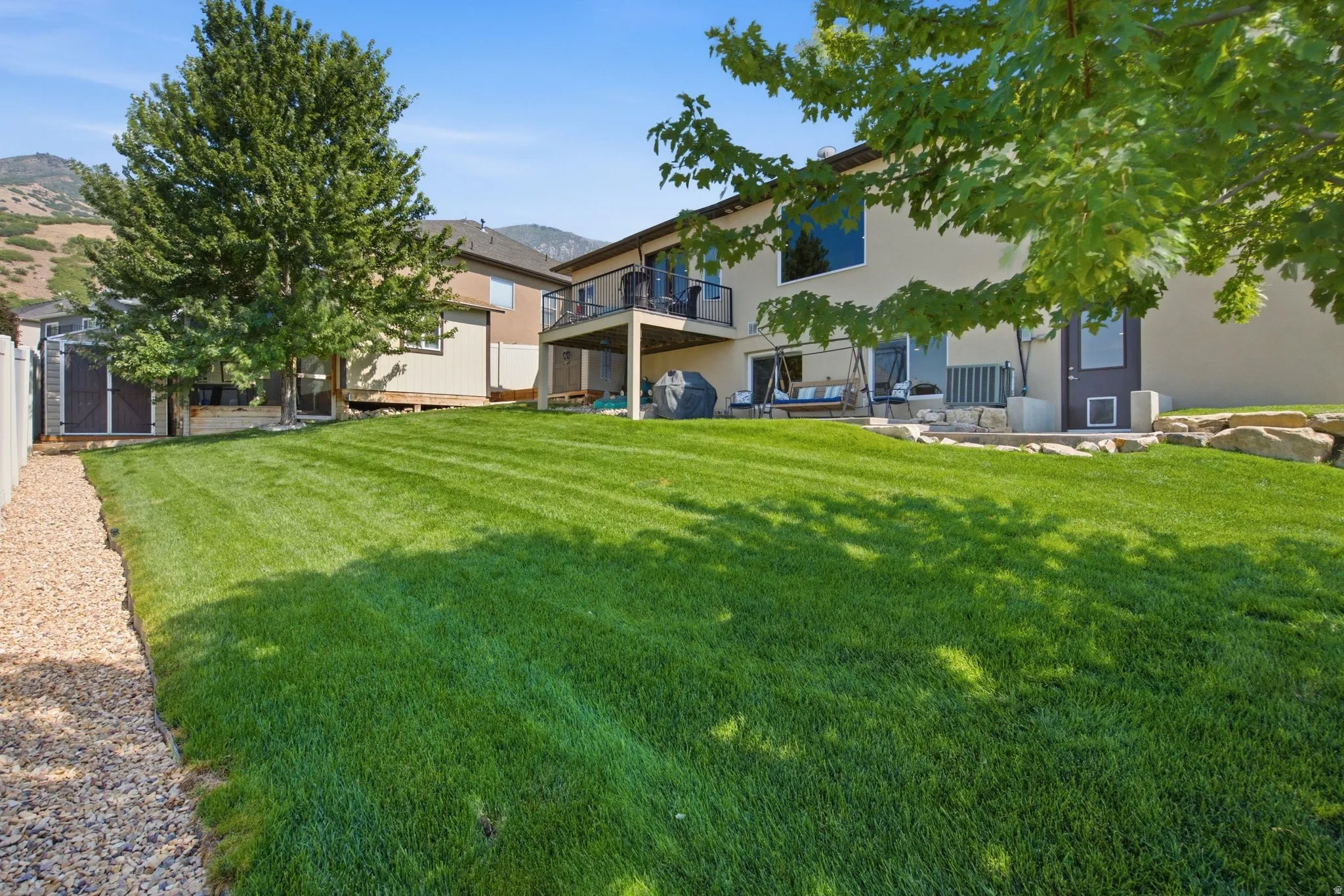 Expansive backyard featuring a manicured lawn, mature trees, and a gravel perimeter