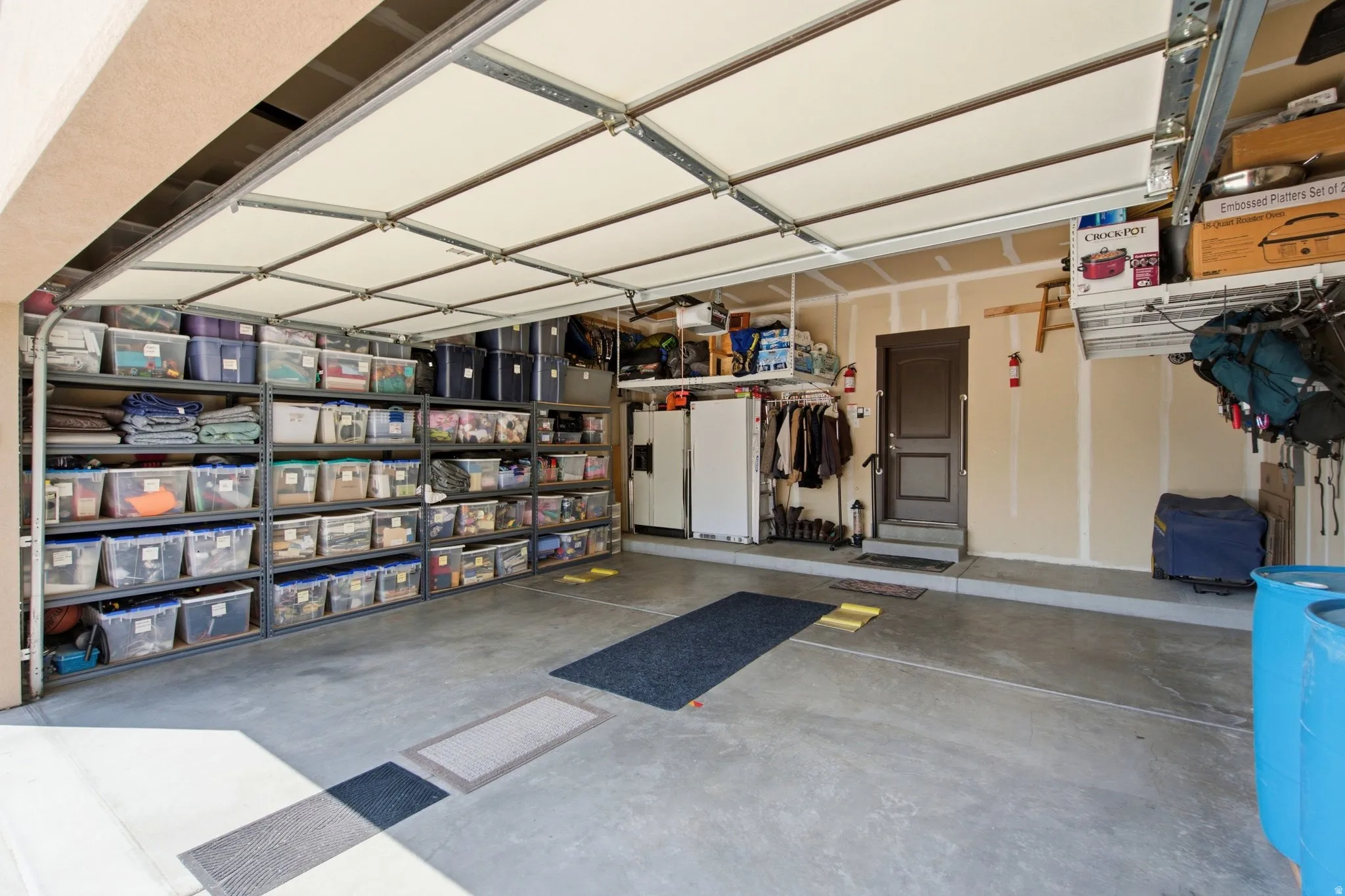 Spacious garage featuring epoxy-coated flooring, extensive wall-mounted storage shelving with multiple compartments, retractable ceiling-mounted door system, and ample overhead lighting
