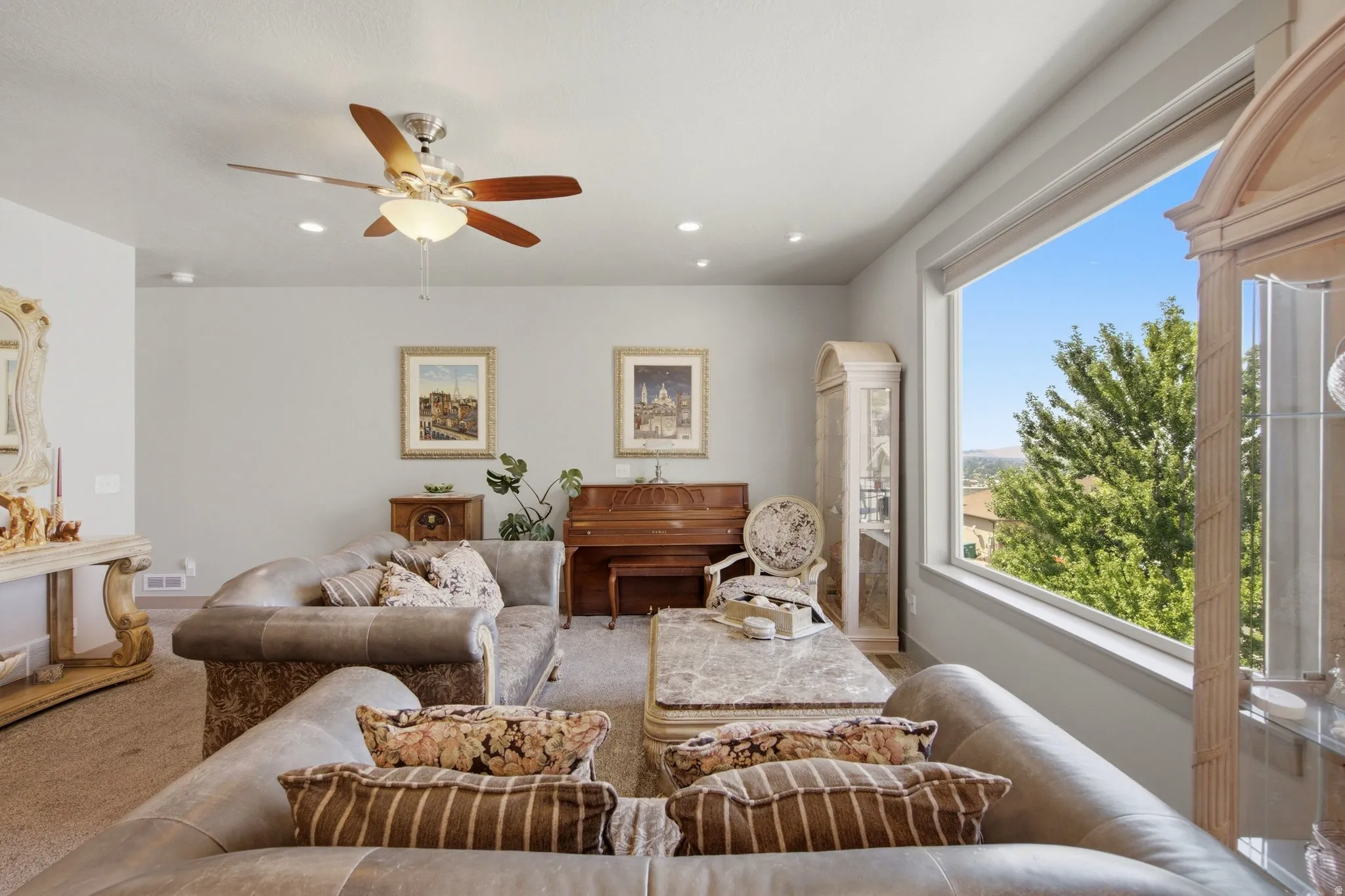 Sophisticated upper-level living room featuring expansive windows with natural light, ceiling fan with integrated lighting, wood-finish flooring, and a wood-burning fireplace with a traditional mantel