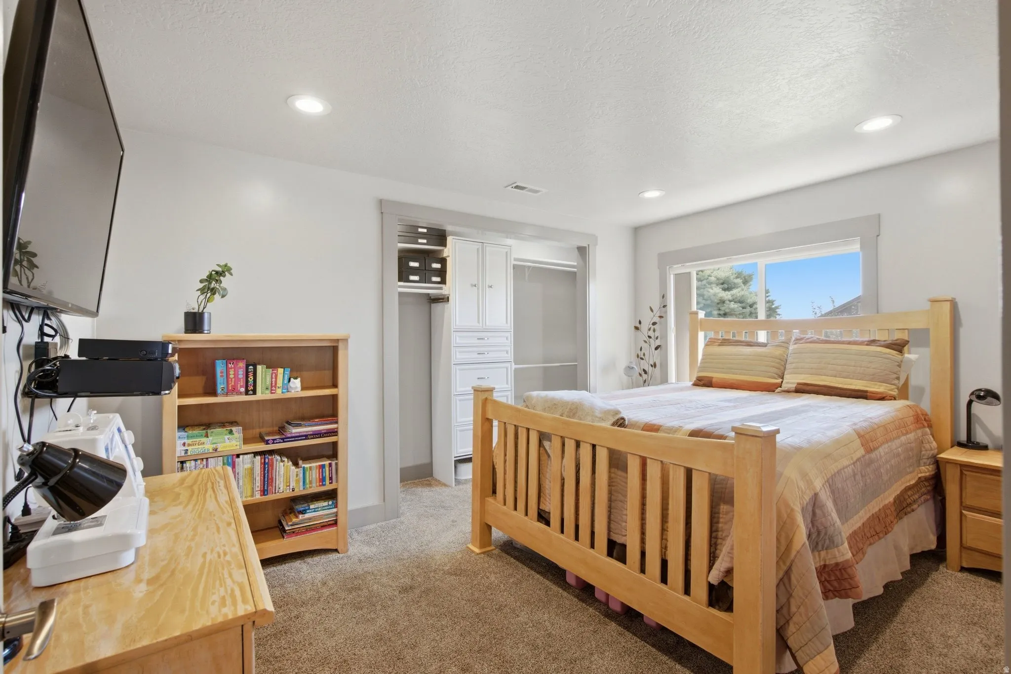 Spacious primary bedroom featuring a wood-frame bed, wood-finish nightstands, and carpet flooring