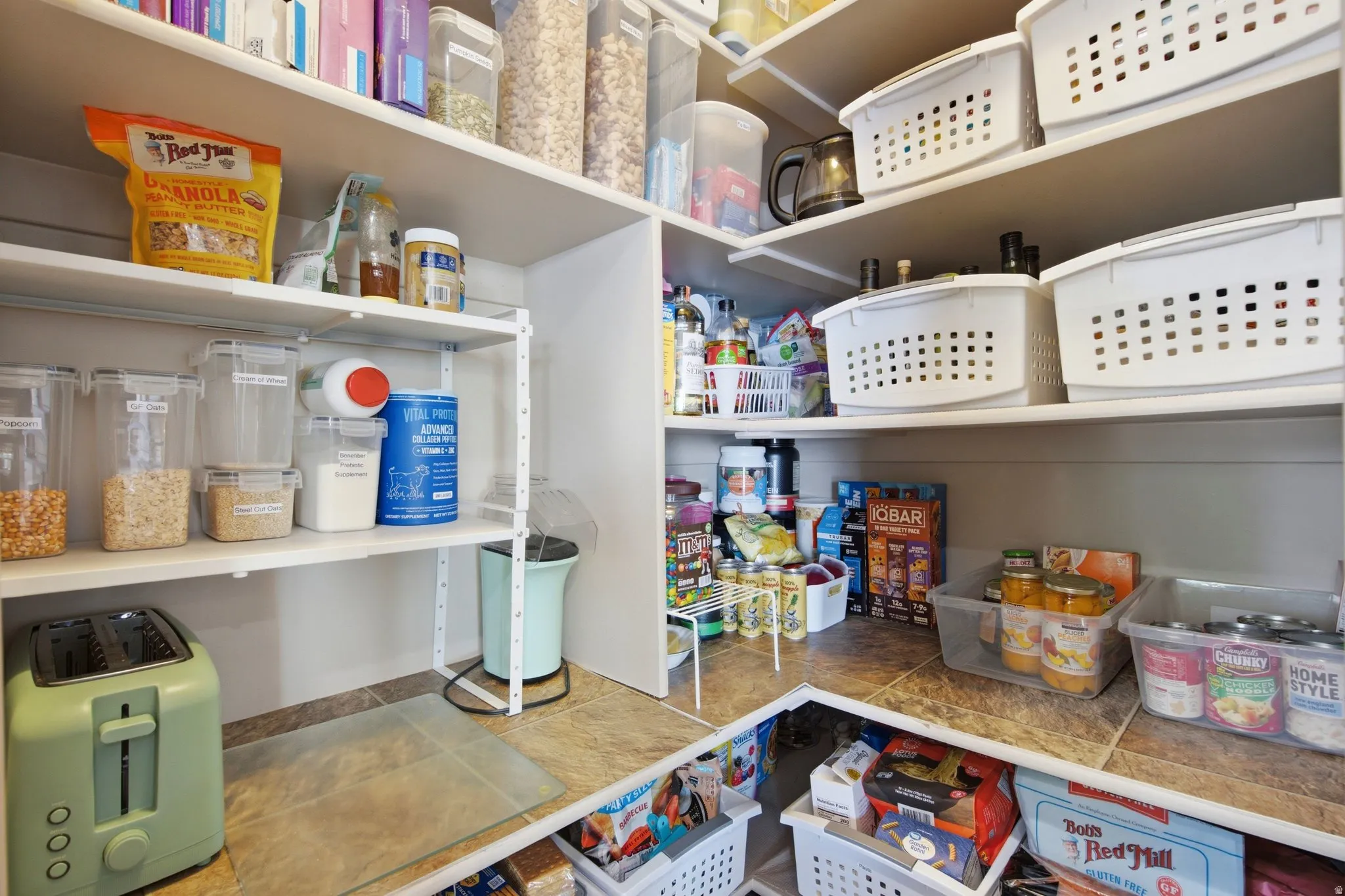 Organized pantry featuring extensive built-in shelving with adjustable white wire and solid shelves, granite-finish countertops, and multiple clear storage containers with labeled organization systems