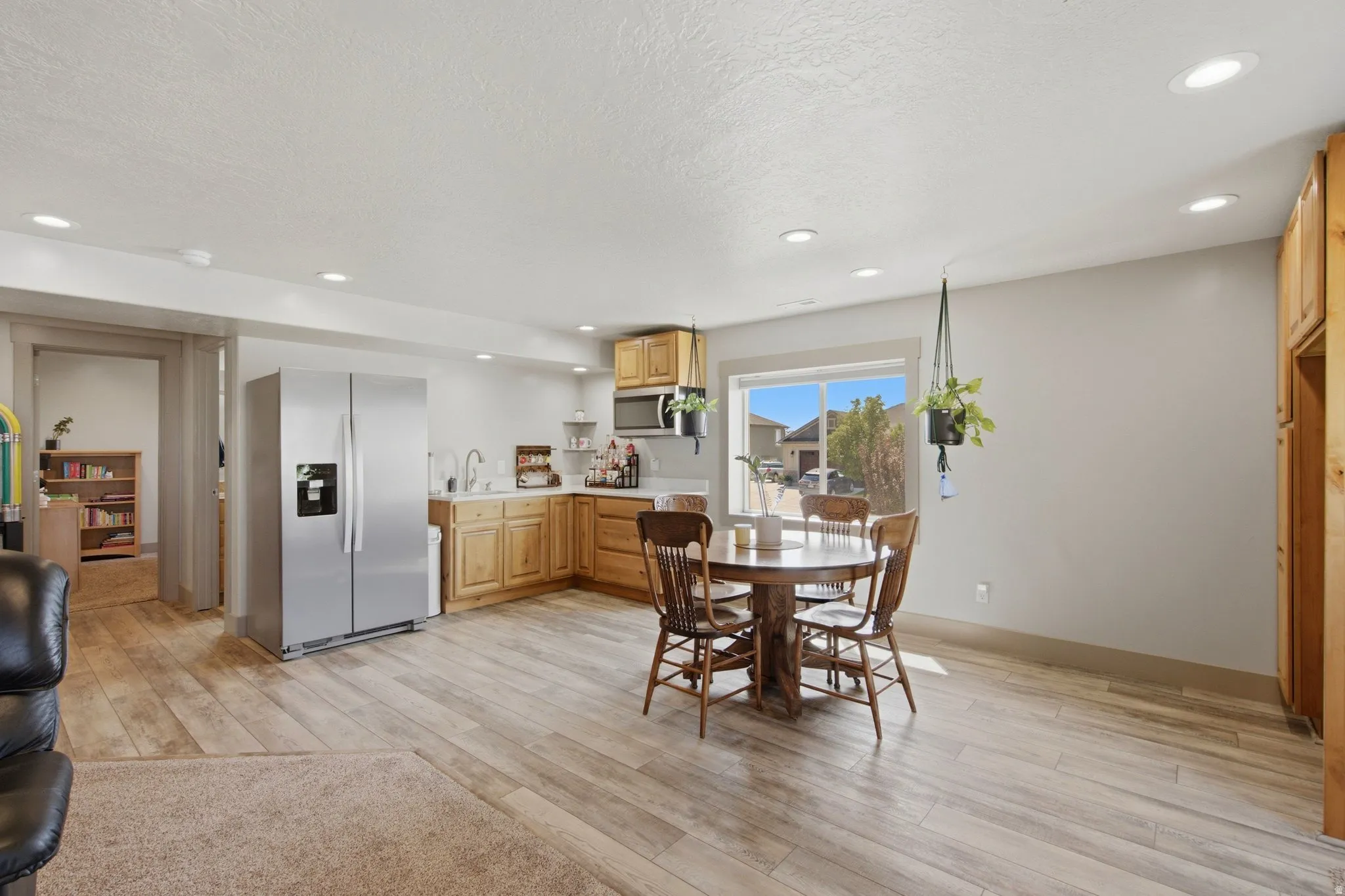 Open-concept kitchen and dining area featuring wood-finish flooring, custom wood cabinetry with stainless steel appliances, recessed ceiling lighting, and a round dining table with seating for four