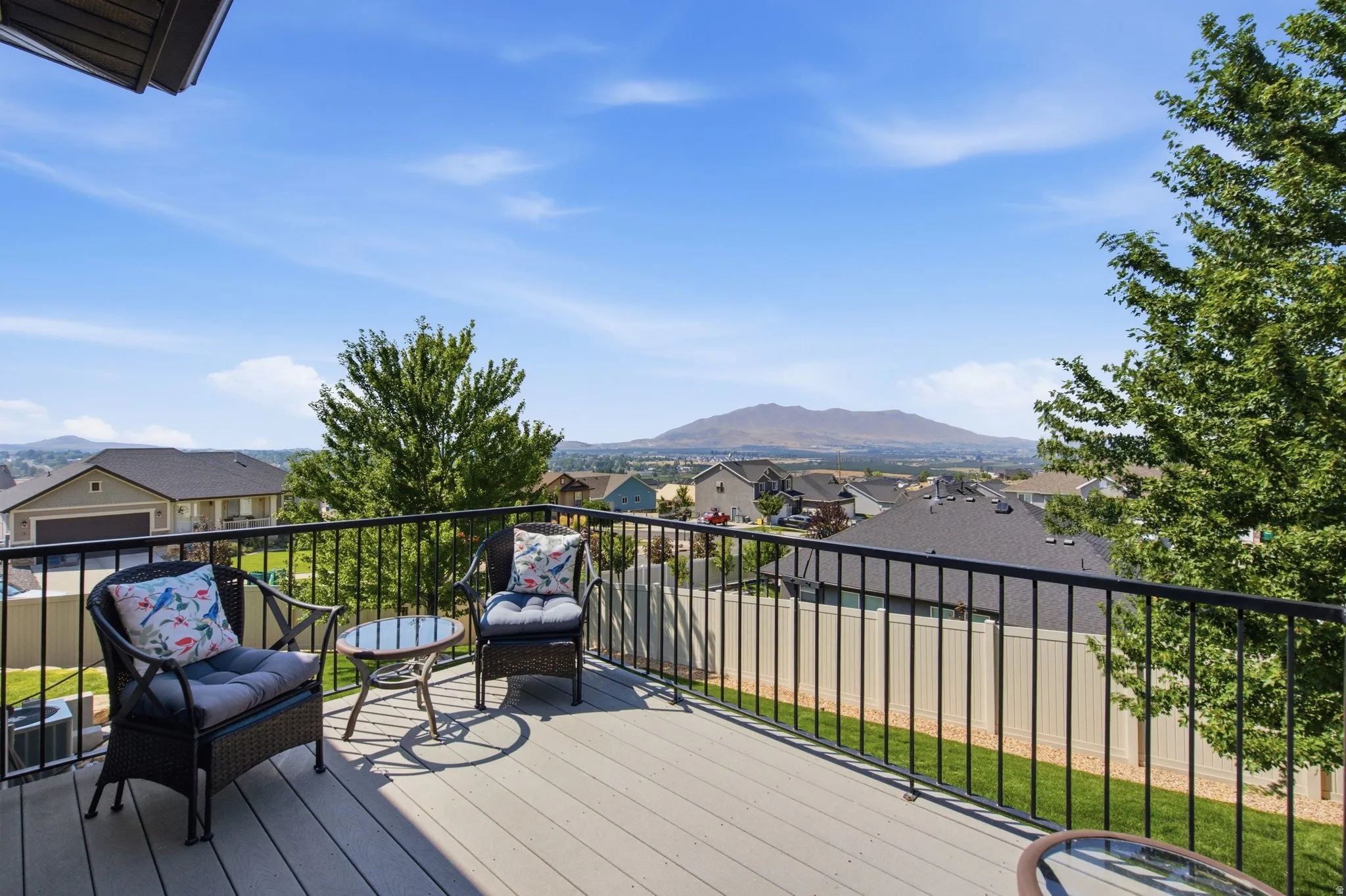 Expansive composite deck featuring composite decking with black metal railing, multiple seating areas, and mature landscaping