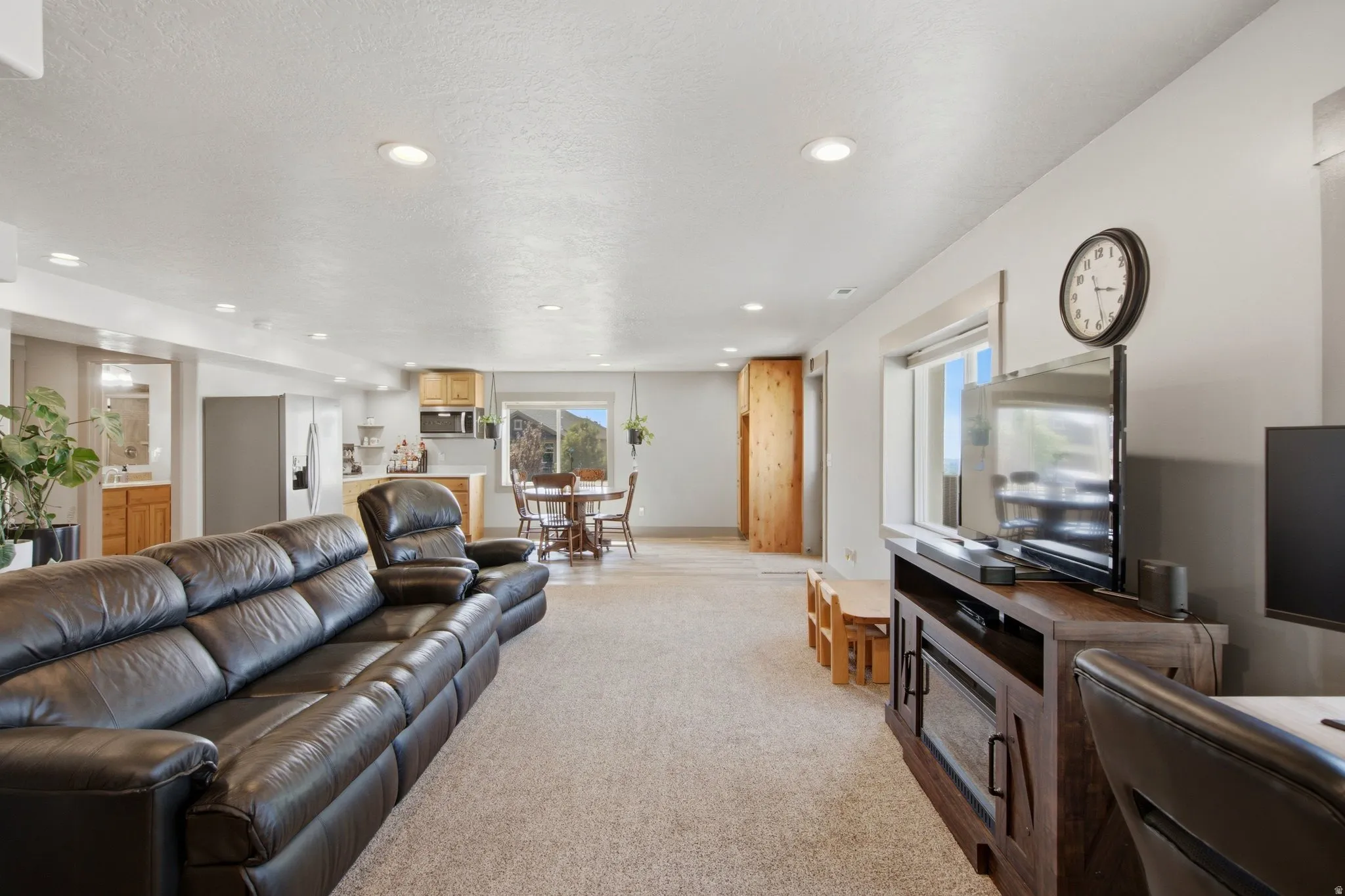 Spacious open-concept living area featuring a leather sectional sofa, recessed ceiling lighting, neutral carpet flooring, and entertainment cabinetry with integrated television