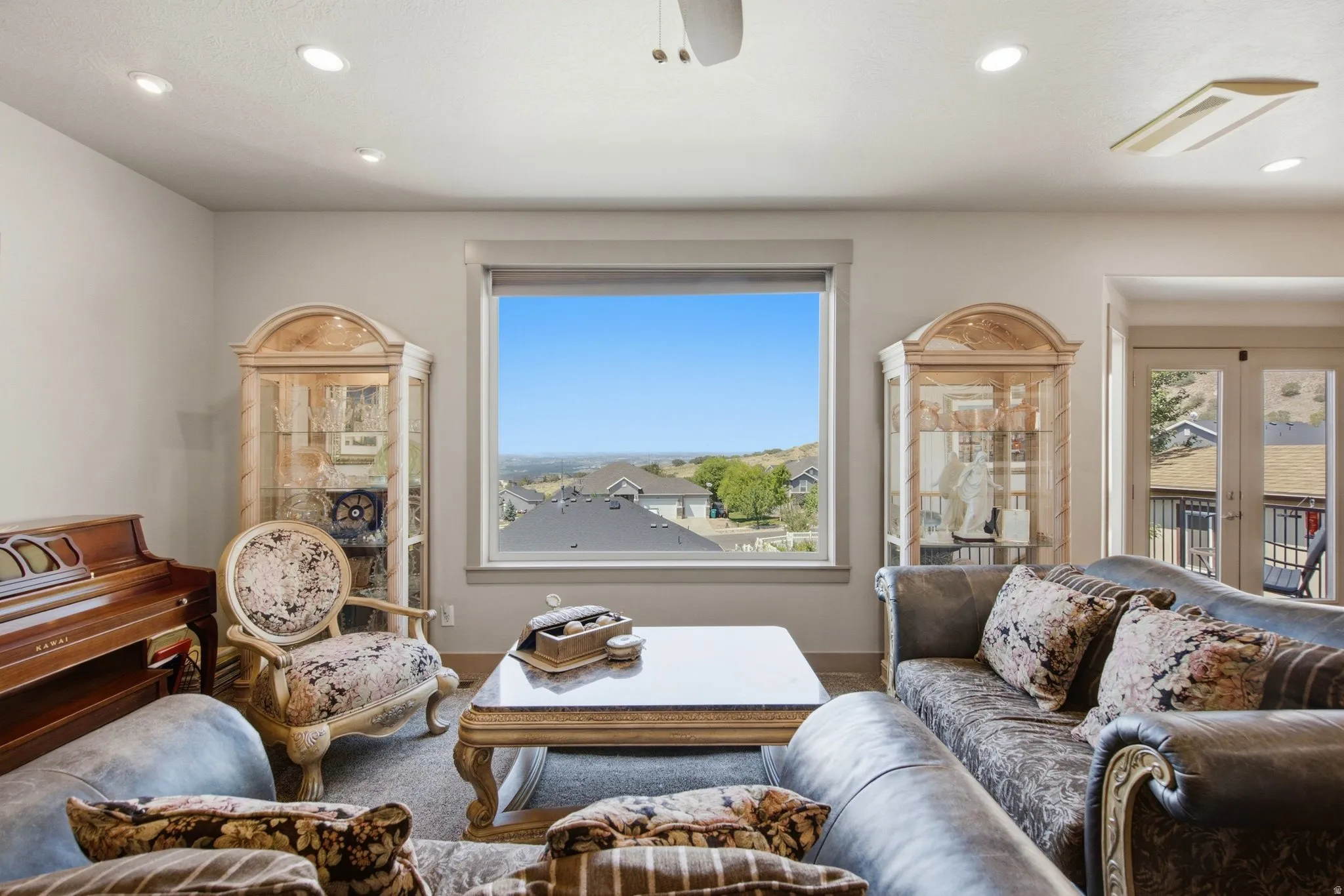 Sophisticated living room showcasing panoramic windows framing expansive landscape vistas, recessed ceiling lighting, hardwood flooring, and elegant furnishings anchored by a wood-finish coffee table