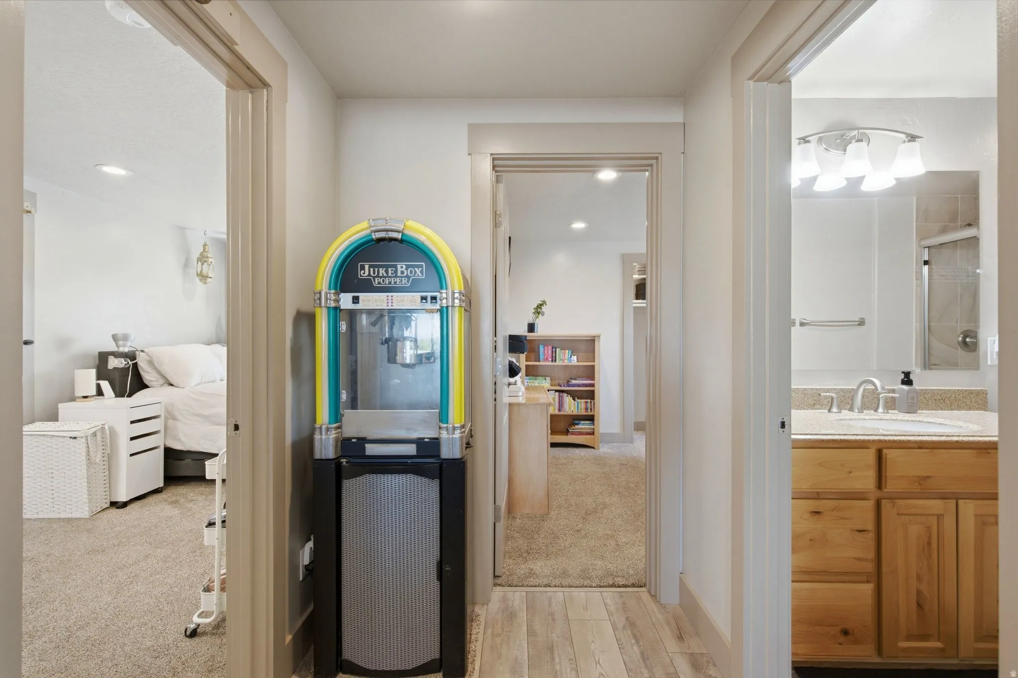 Hallway featuring multiple room access points, including a bedroom with carpeted flooring, a bathroom with wood-finish cabinetry and vessel sink, and a utility area with a retro-style beverage cooler