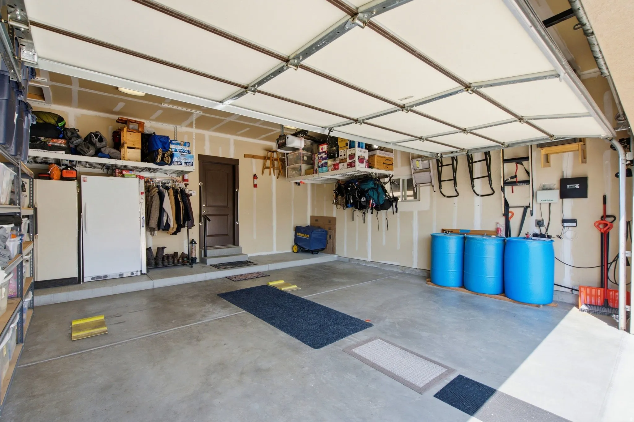 Spacious garage featuring epoxy-coated concrete flooring, extensive wall-mounted storage shelving, overhead LED lighting, and generous ceiling height with exposed structural framing