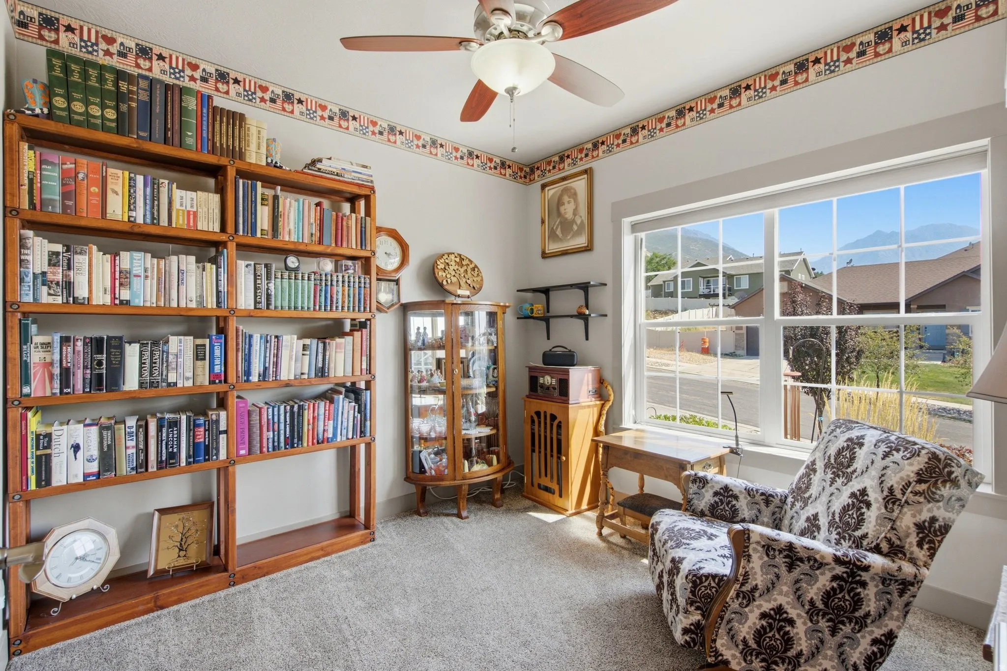Comfortable den featuring extensive built-in wood shelving with display cubinetry, ceiling fan, and large multi-pane windows framing scenic mountain vistas