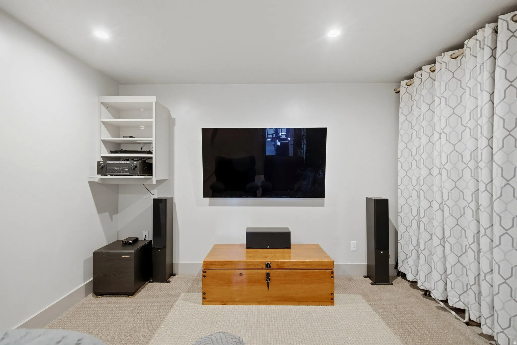 Dedicated Media Room featuring a wall-mounted flat-screen display, recessed ceiling lighting, built-in wall shelving with integrated storage, tall speaker towers, and neutral carpet flooring