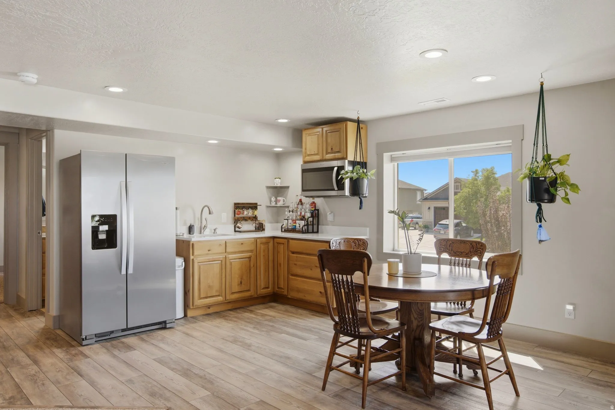 Bright, open kitchen and dining area featuring wood cabinetry, stainless steel appliances including a side-by-side refrigerator, and wood-finish flooring throughout