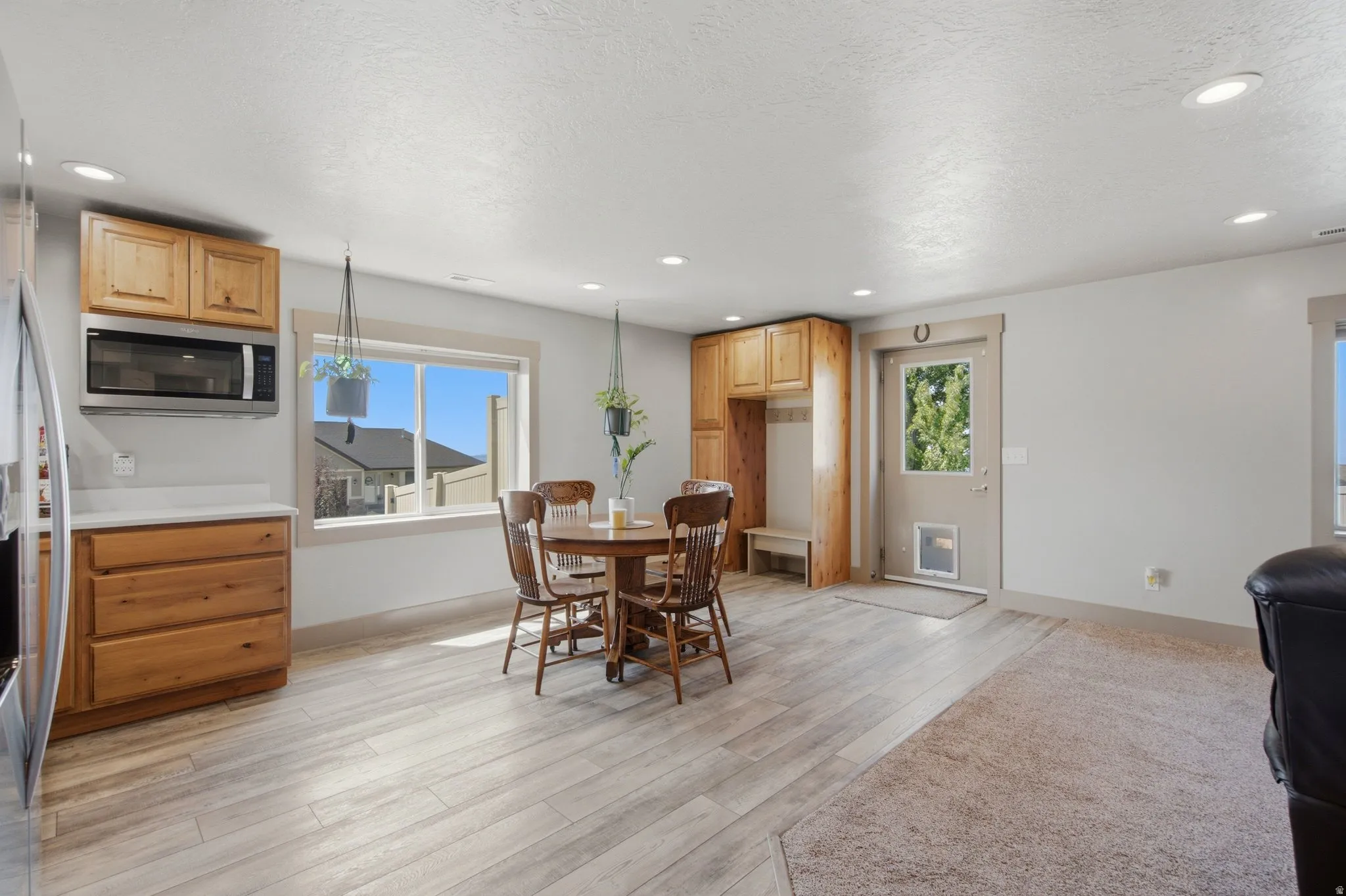 Spacious open-concept living area featuring wood-finish flooring throughout, a round dining table with seating for four, and abundant natural light from large windows