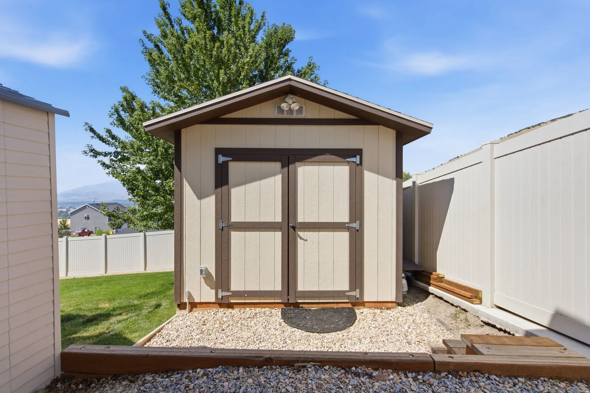 Charming storage shed featuring a peaked roof with decorative gable vent, double barn-style doors with dark trim, and a gravel foundation base