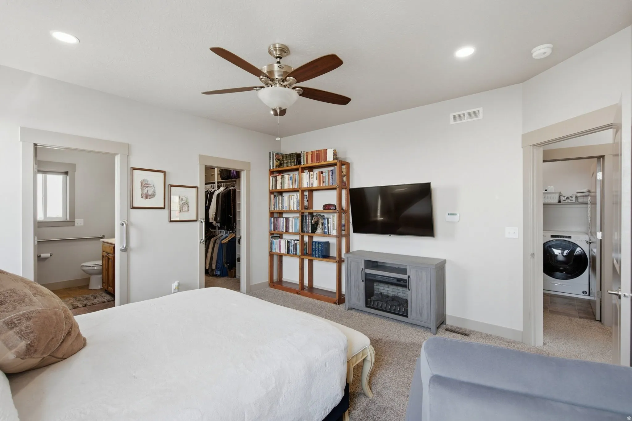 Spacious primary bedroom featuring neutral carpeting, a ceiling fan with brushed nickel finish, and abundant natural light from recessed fixtures