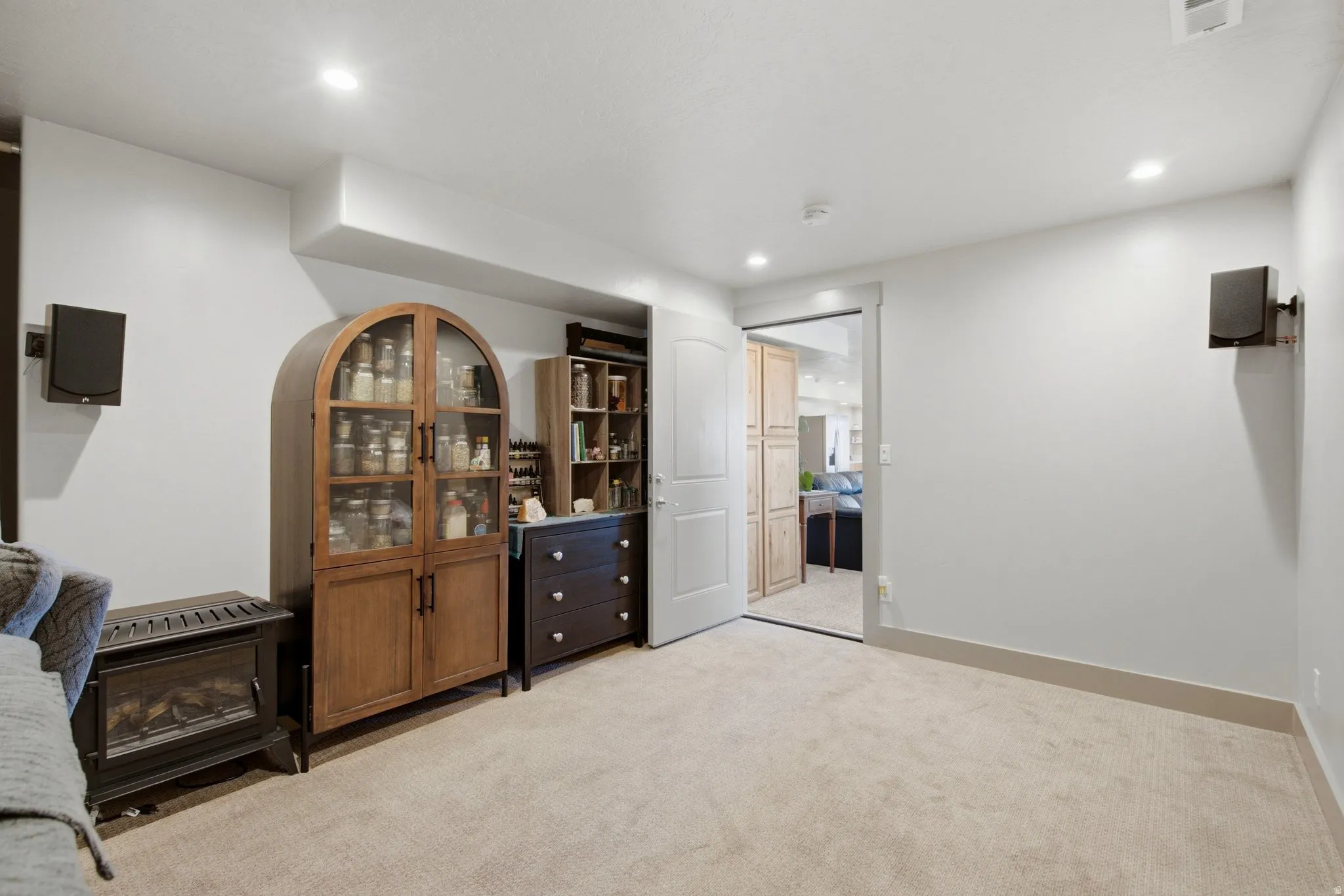 Spacious recreation room featuring neutral carpeting, recessed lighting, and a wood-finish display cabinet with glass doors and matching dark wood dresser