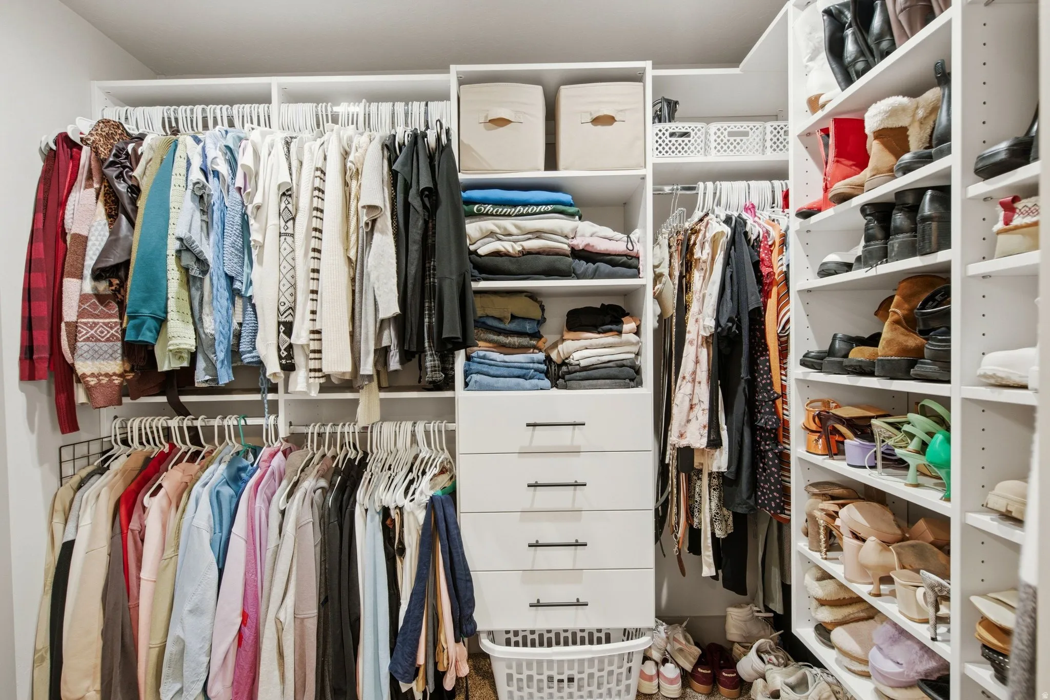 Spacious walk-in closet featuring custom white cabinetry with multiple shelving units, built-in drawers, and dual clothing rods accommodating an extensive wardrobe