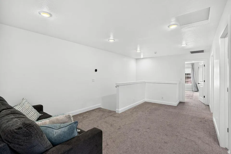Carpeted loft area featuring white walls, recessed ceiling lighting, and a white half-wall railing