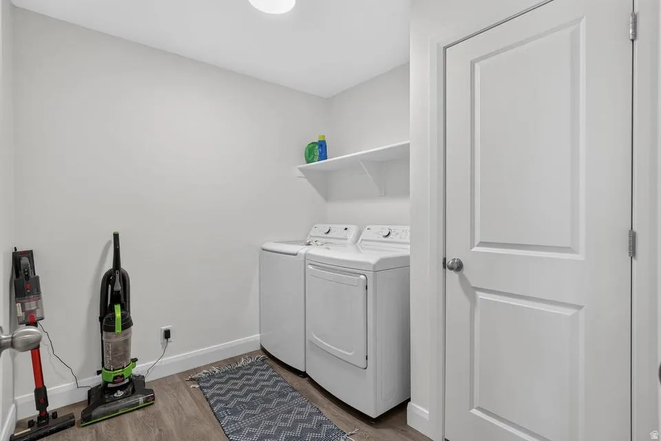 Modern laundry room featuring side-by-side washer and dryer with white finish, built-in shelving with storage capacity, wood-finish flooring, geometric patterned area rug, and a two-panel white door entry