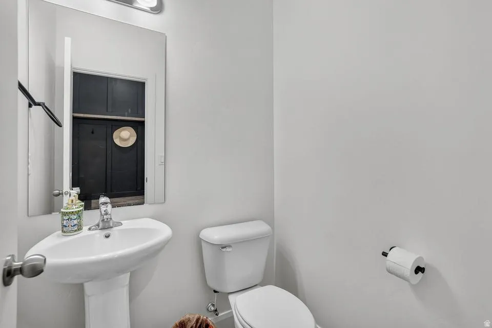 Clean and functional half bath featuring a pedestal sink with chrome faucet, white ceramic toilet, and neutral wall finishes