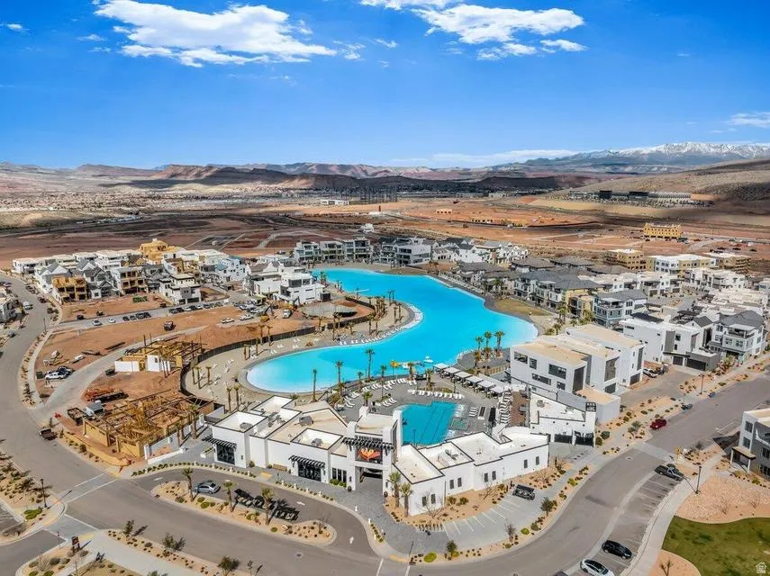 Aerial view of a sprawling resort-style community featuring a striking lagoon-form swimming pool as the centerpiece, surrounded by whitewashed residential architecture with terracotta-toned roofing